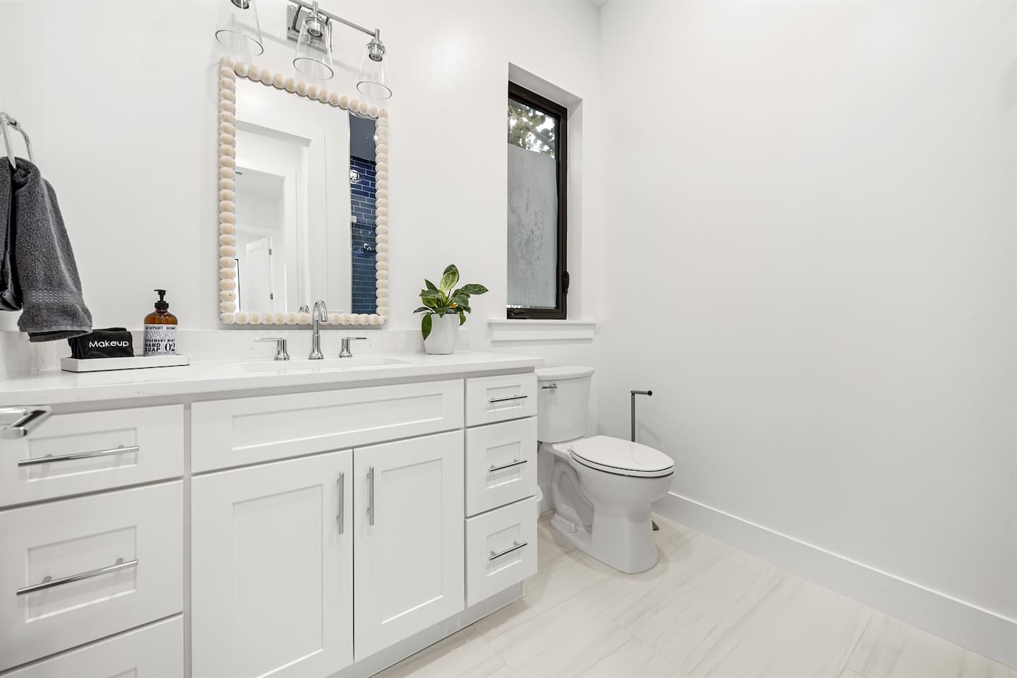Step into this modern bathroom featuring a toilet with a window above, a sleek sink and faucet with a storage drawer, a wide mirror, a neatly placed towel, and bright lighting for a refreshing ambiance