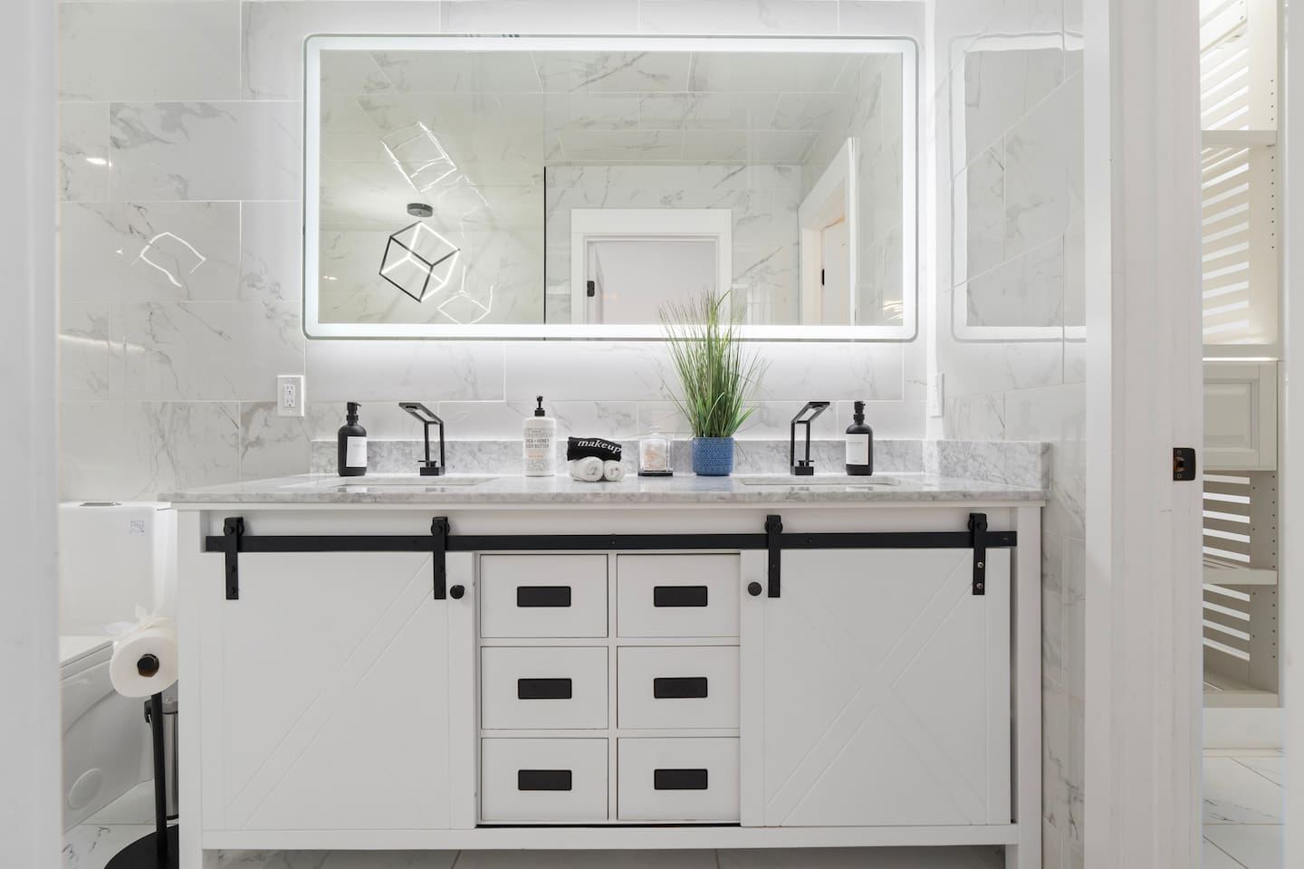 Double vanity with barn-style cabinet doors and a glowing backlit mirror.

