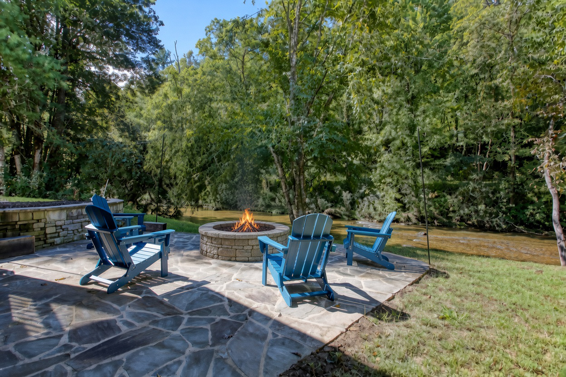 Blue Adirondack chairs surround the stone fire pit at Robbin’s Nest on Snowbird Creek—a welcoming spot to spend an evening outdoors.