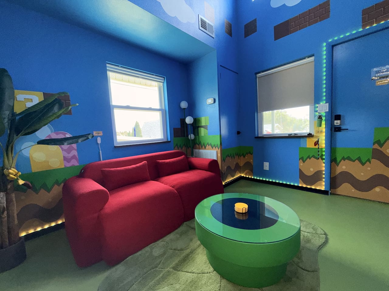 Relax on the bright red sofa in our Mario-themed living room at Mario's Mini Mansion, near Orlando, FL. Prop up your feet on the green pipe table amid hand-painted clouds, hills, and classic Super Mario decor. Ideal for cozy evenings!