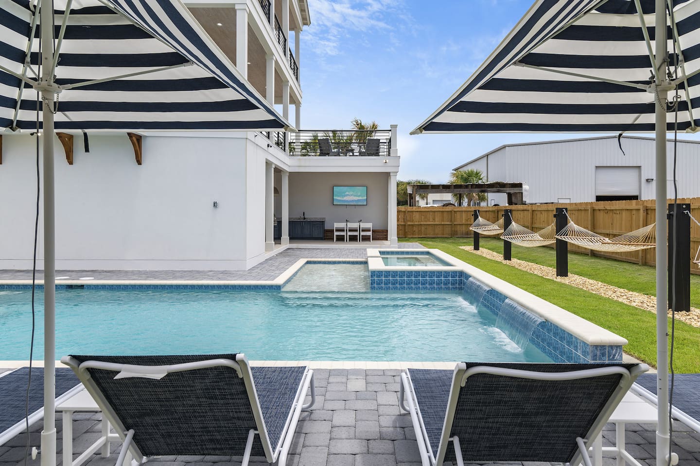 Spacious outdoor area featuring a large pool, hot tub, loungers, hammock, and umbrellas.