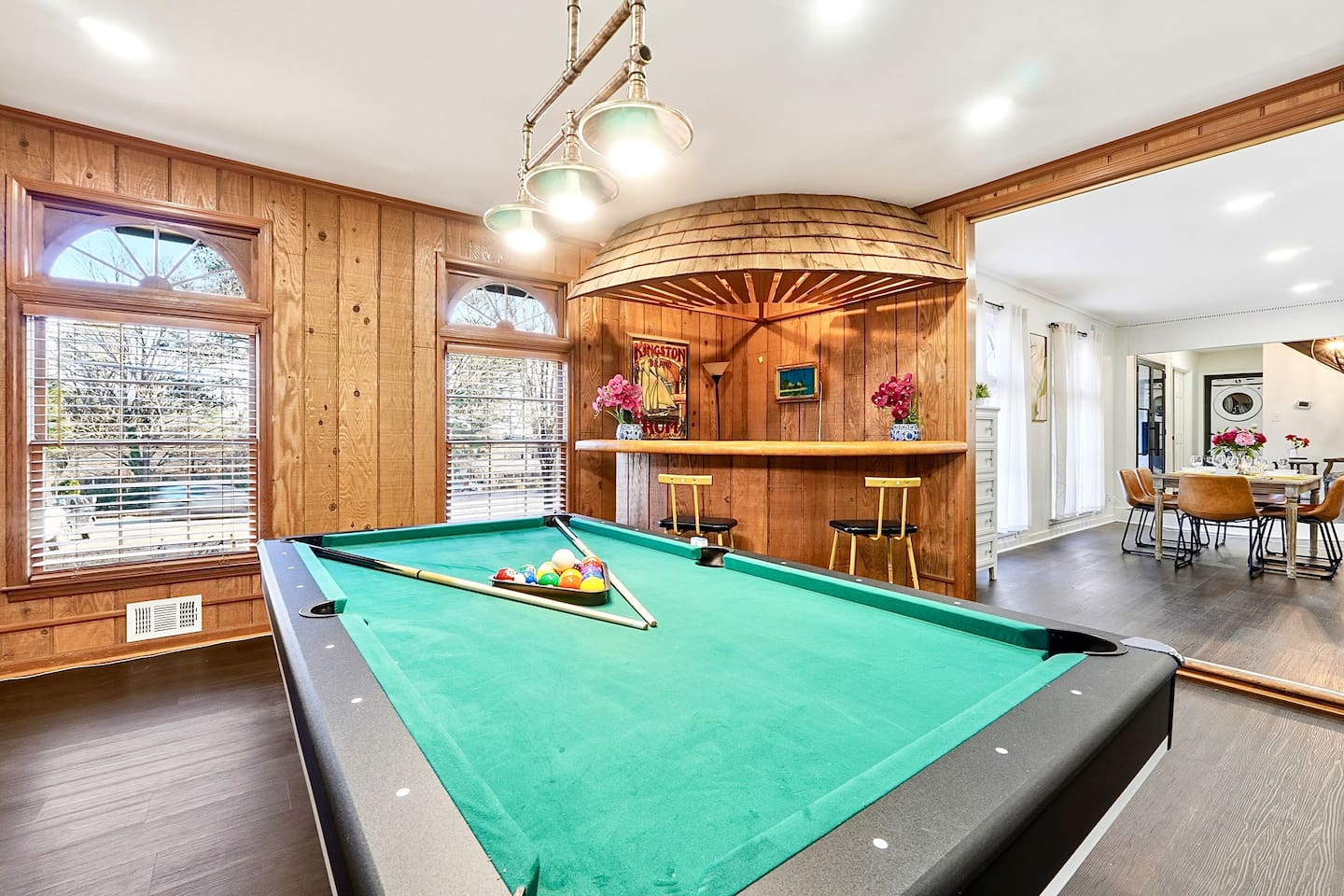 Enjoy this main-floor game room near the side entrance featuring a convertible pool and ping-pong table, a custom curved wood bar, and a Roku powered smart TV—ideal for entertaining and casual gatherings.