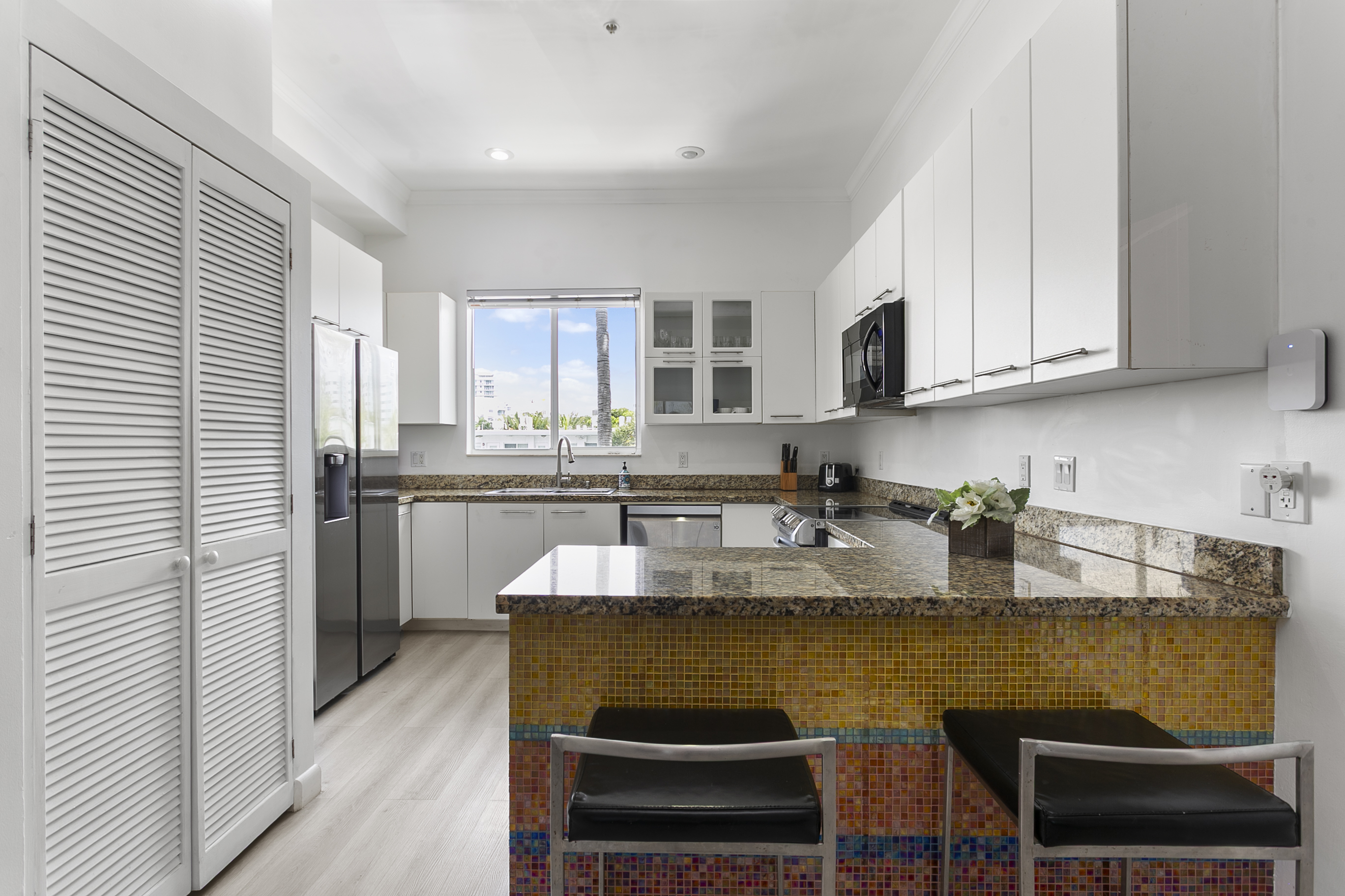 Mosaic tiled kitchen with modern appliances and breakfast counter. LG laundry tower behind closet doors