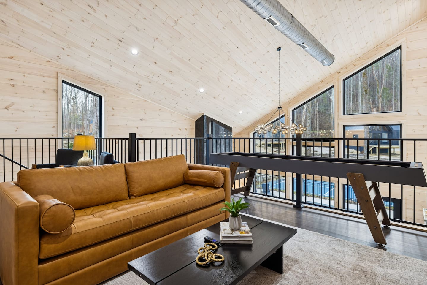 Relax in style on this stunning loft balcony, featuring a premium leather lounge, custom shuffleboard, and a large TV for movie nights. It’s the ultimate entertainment hub, stocked with board games and framed by floor-to-ceiling forest views.