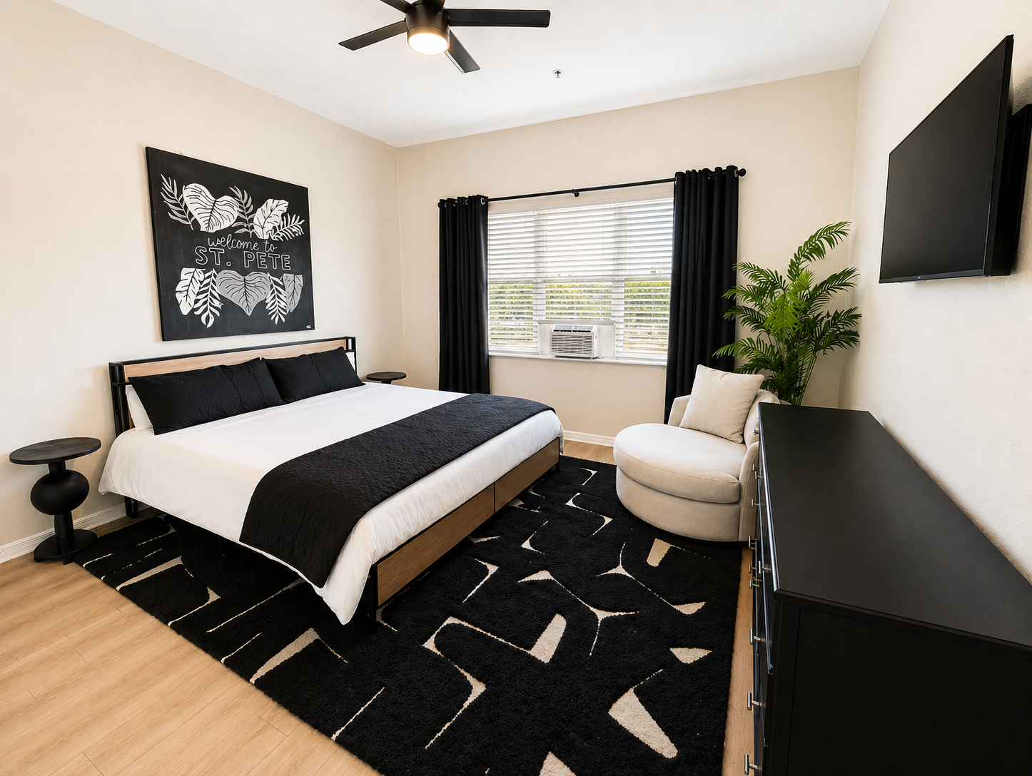 Stylish and cozy bedroom featuring a comfortable queen bed, soft linens, and modern décor. Enjoy natural light, a wall-mounted TV, and a relaxing reading chair—perfect for unwinding after a long day.