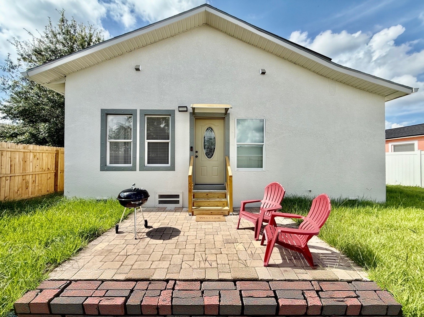 The fully fenced yard offers added privacy, while the red Adirondack chairs and charcoal grill invite you to kick back and savor the moment.
