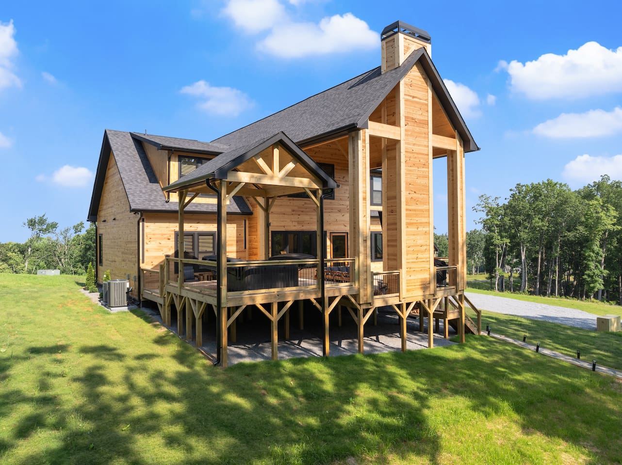 Admire the stunning craftsmanship of the cabin from this side angle, with its exposed beams, high peaks, and inviting hot tub area nestled under a charming pavilion.