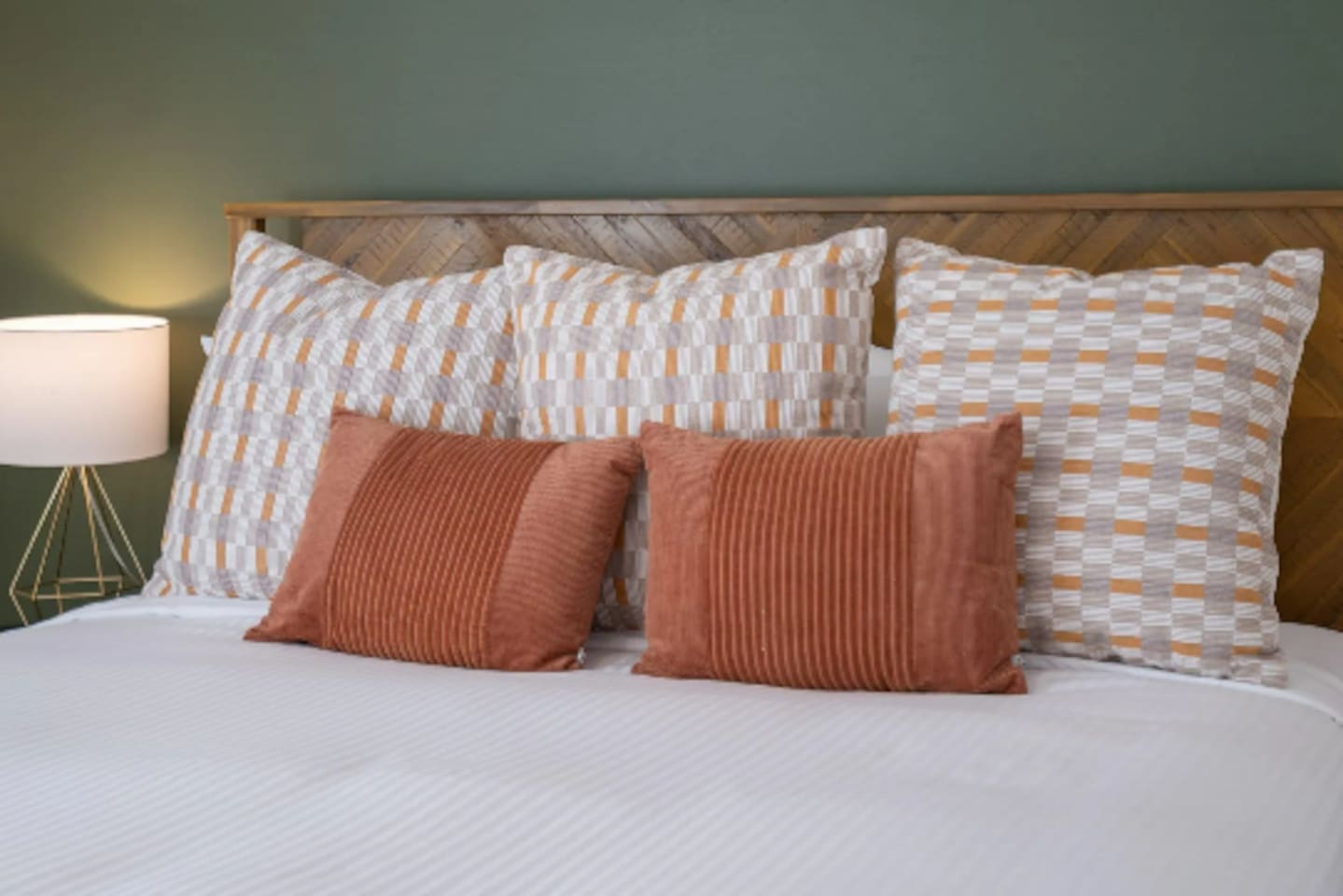 Layered pillows in warm rust and neutral patterns turn simple white bedding into something that feels curated and cozy.