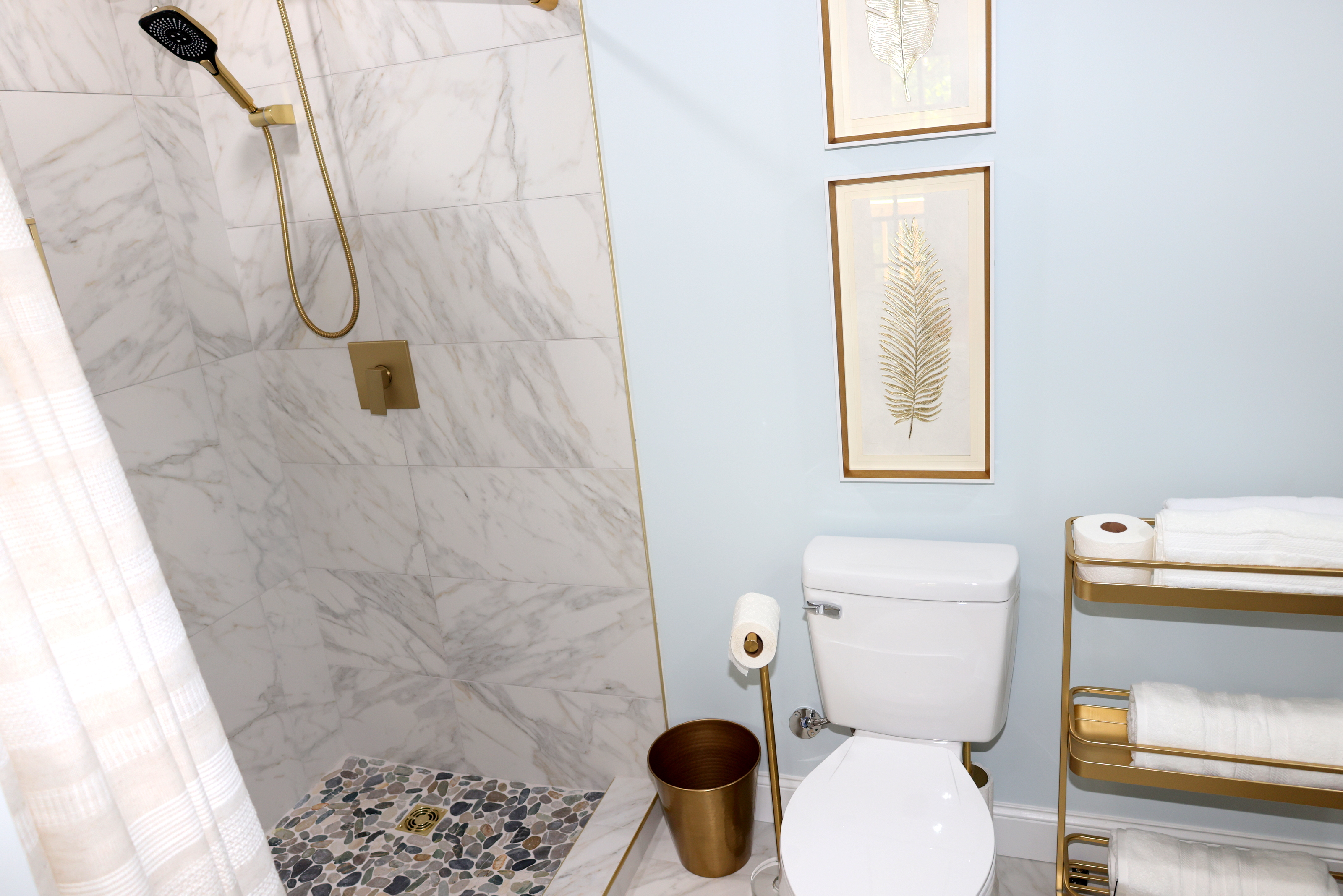 Updated bathroom with walk-in shower, marble-style tile, gold accents, and fresh towels