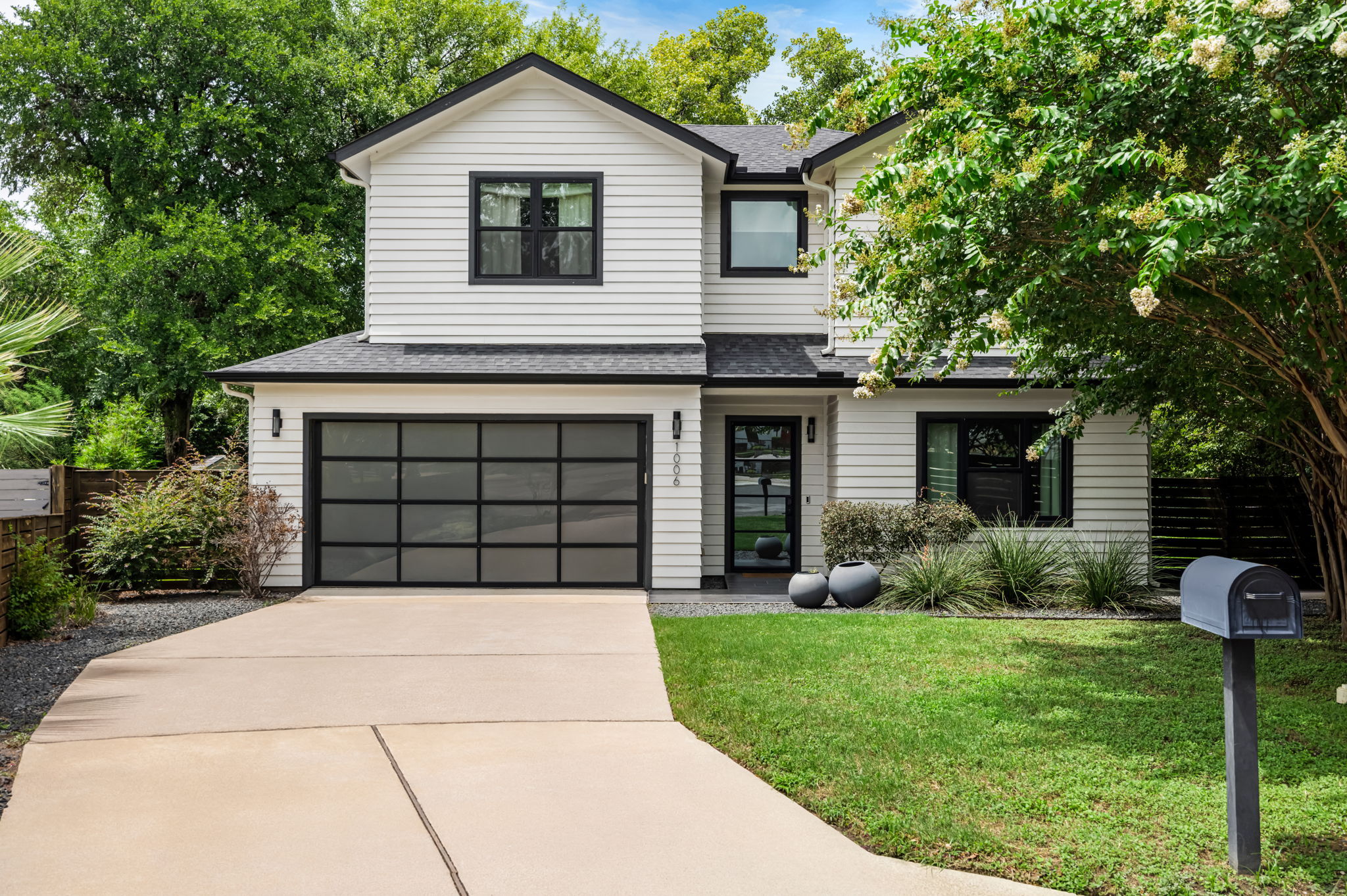 Beautifully landscaped modern farmhouse exterior with a spacious driveway, mature trees, and lush greenery — welcoming curb appeal from the moment you arrive.
