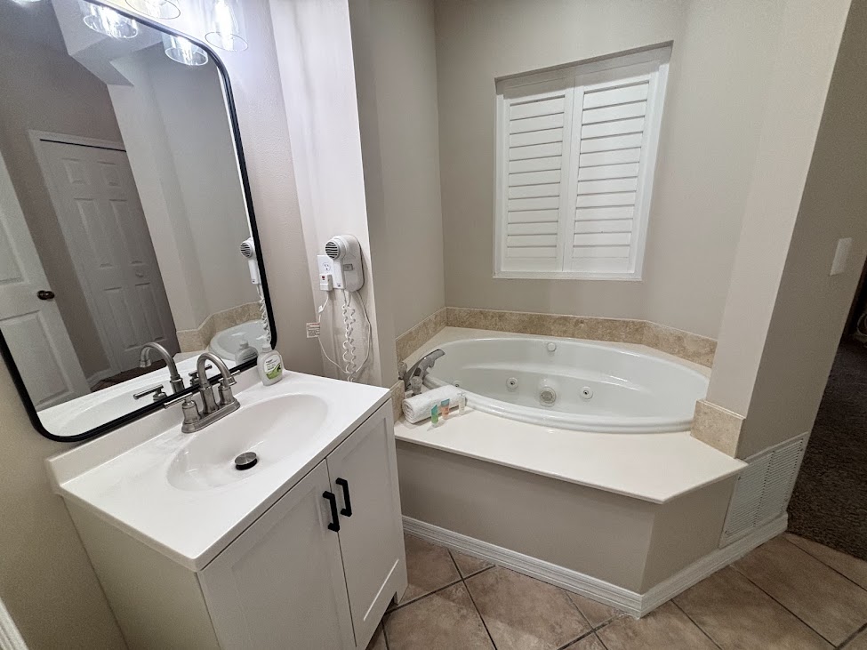 Bathroom with vanity storage, soaking tub, tile flooring, and bright natural light from the window.