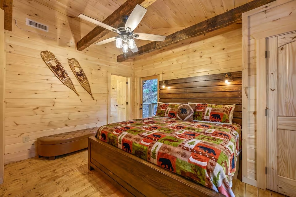 The top-level king bedroom at Bear Paws Cabin is a private suite with its own Smart TV and attached full bathroom &mdash; ideal for parents or older kids who want their own floor. Exposed timber beams and log cabin walls make this a Smoky Mountain bedroom great