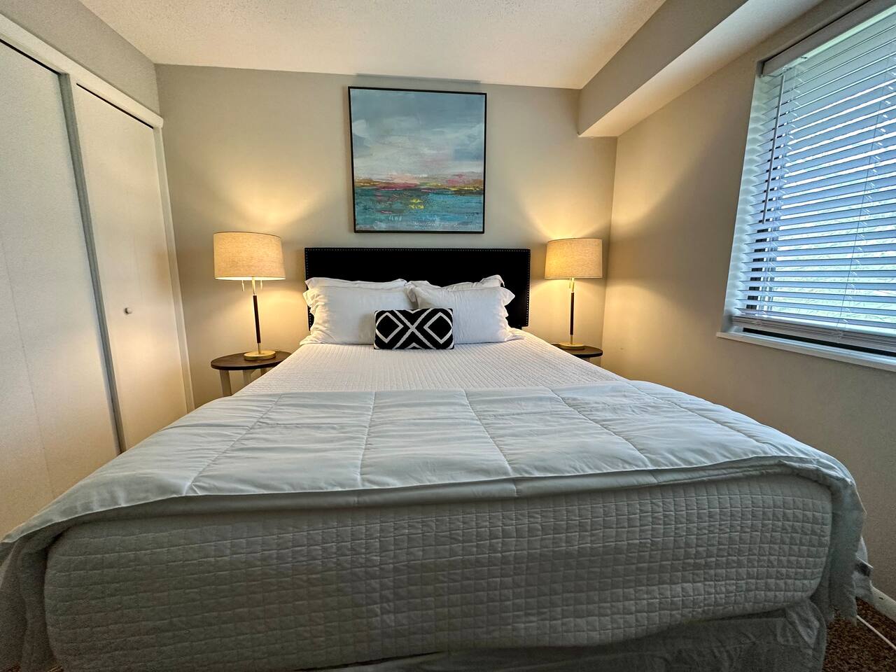 Cozy and peaceful bedroom with a comfortable bed, soft lighting, and room darkening blinds for restful sleep. Stylish modern touches and soothing artwork create a relaxing atmosphere—ideal for unwinding after a busy day or enjoying a quiet morning.