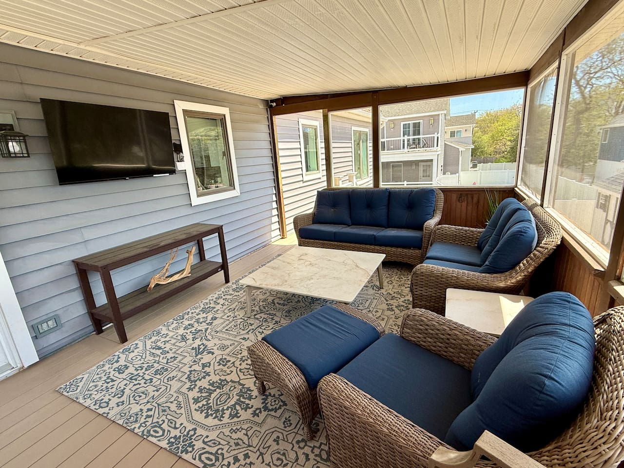 Enjoy ultimate relaxation on this elegant screened-in porch. Featuring comfortable wicker seating with plush blue cushions and a wall-mounted TV, it's the perfect luxury space for unwinding.