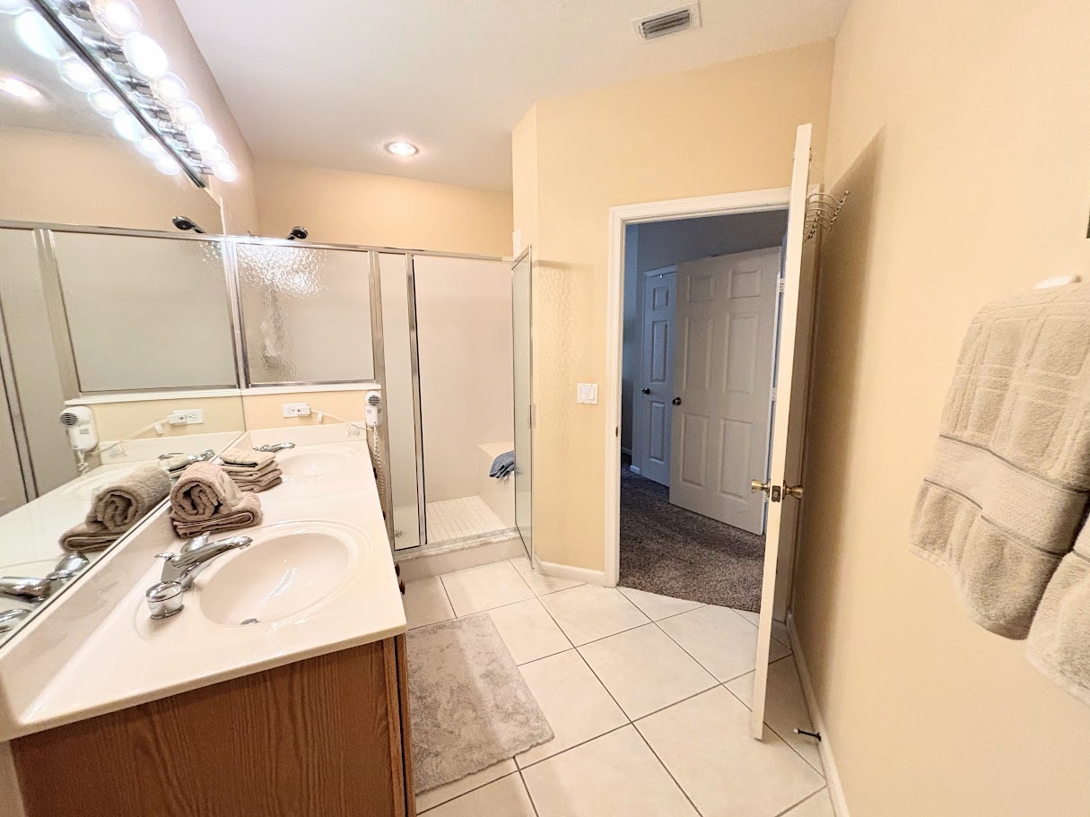 Bright bathroom with spacious vanity, large mirror, tile flooring, and a walk-in shower with glass doors.