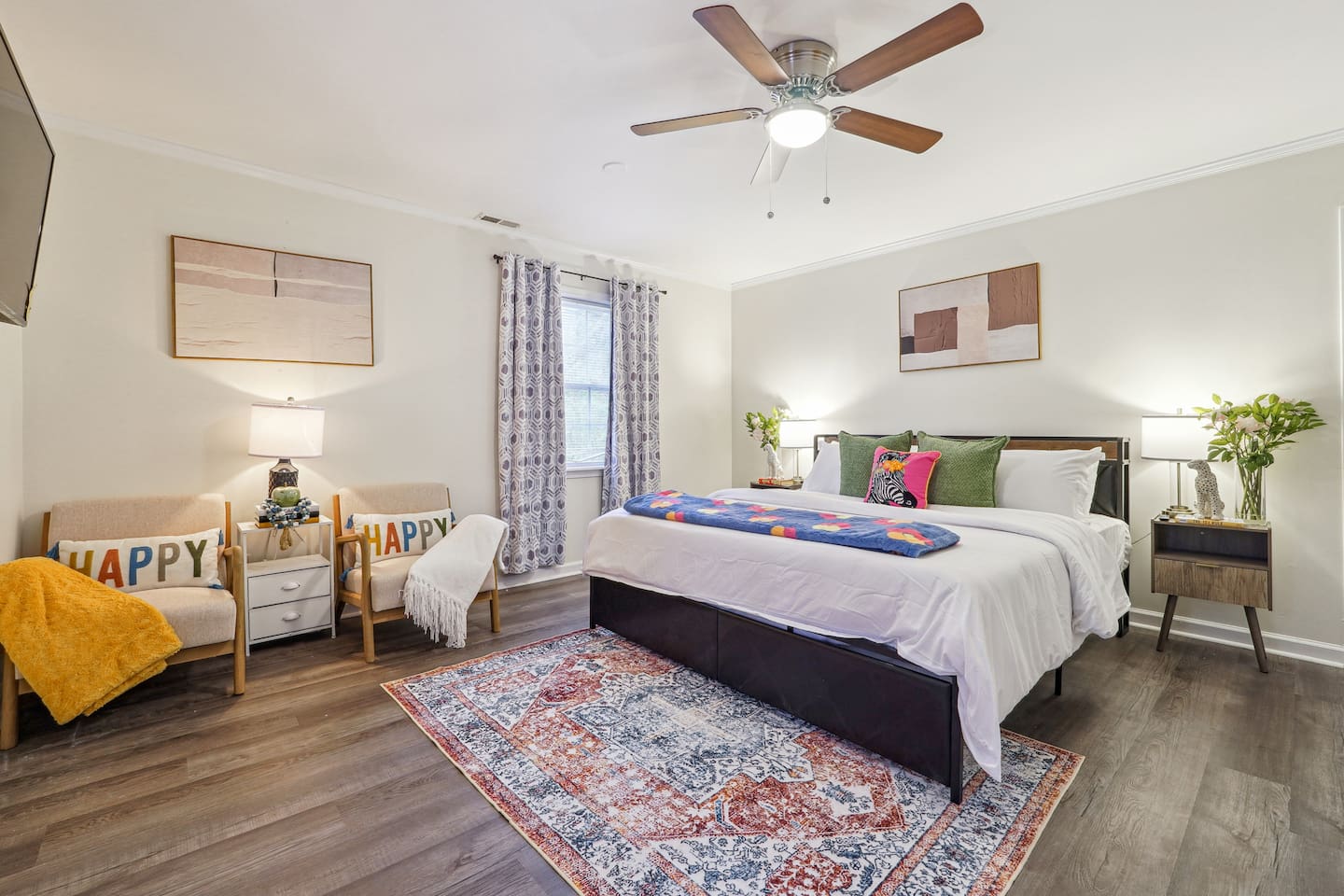 A cozy bedroom featuring a King bed, a ceiling fan, two windows, two chairs, a bedside shelf, a bedside lamp, and a TV — a comfortable space to relax and unwind.
