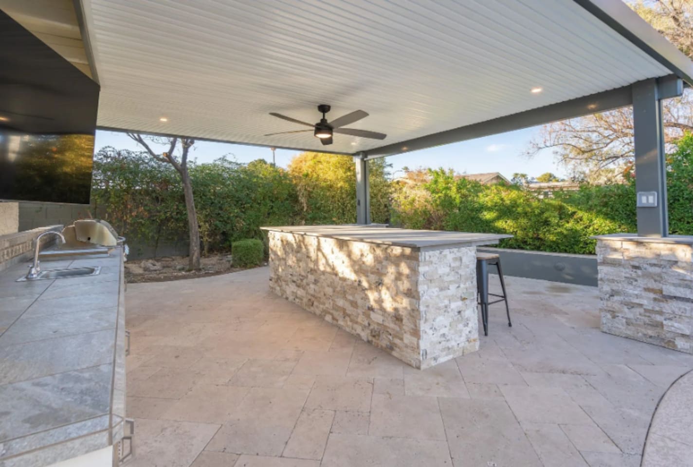 A stone-clad bar counter offers plenty of space to gather outdoors, shaded and ready for entertaining.
