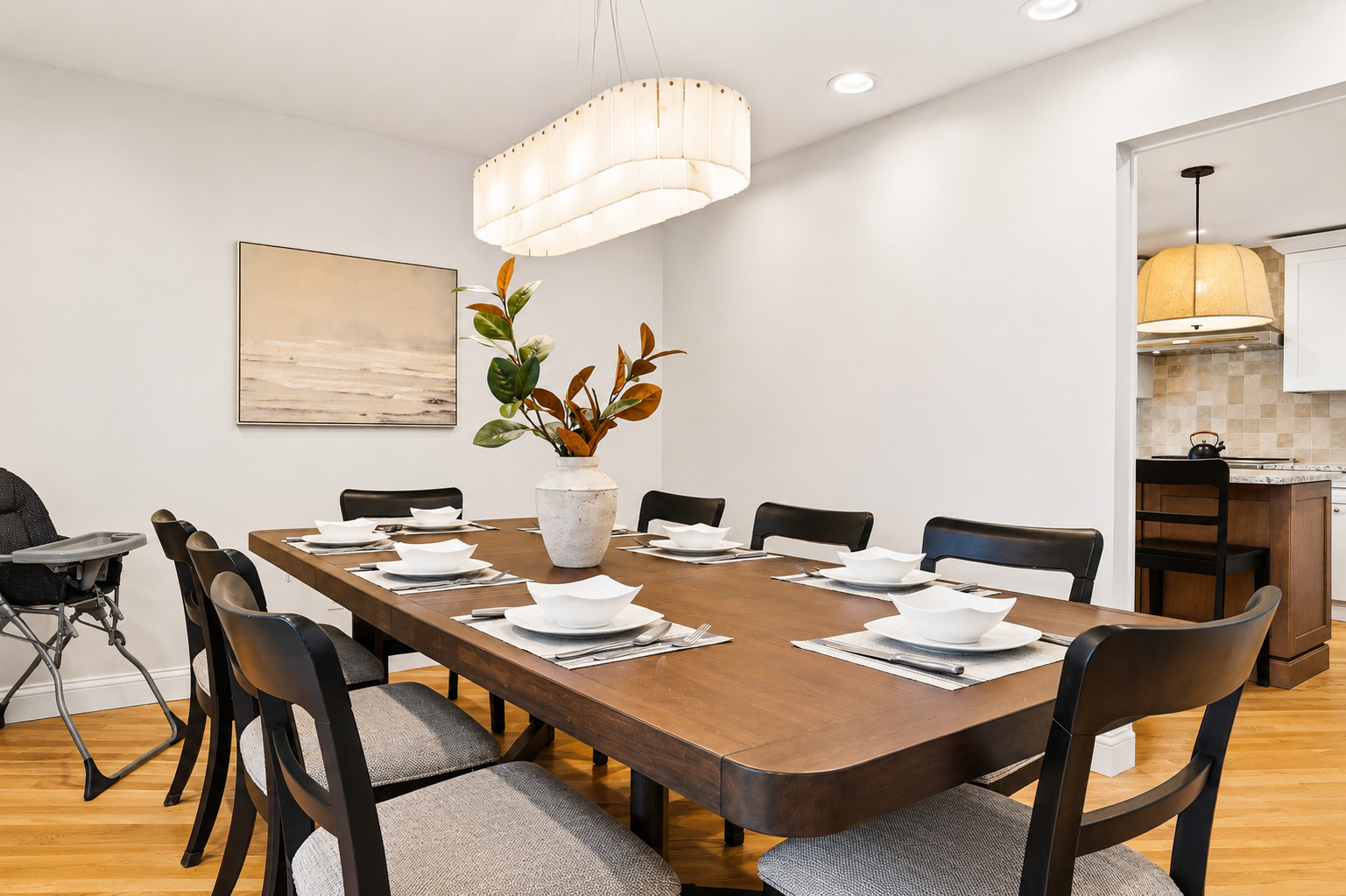 Elegant dining area with a large table, modern seating, and statement lighting. Clean, stylish space perfect for family meals or group gatherings in a bright, upscale setting.