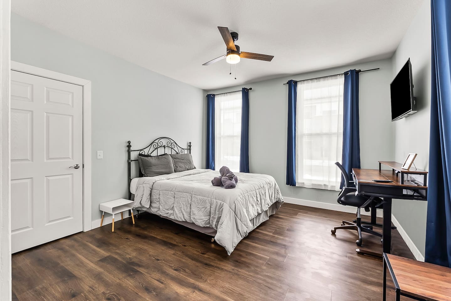 Spacious primary bedroom featuring a comfortable queen-size bed, high ceilings, and warm natural light & work space area.