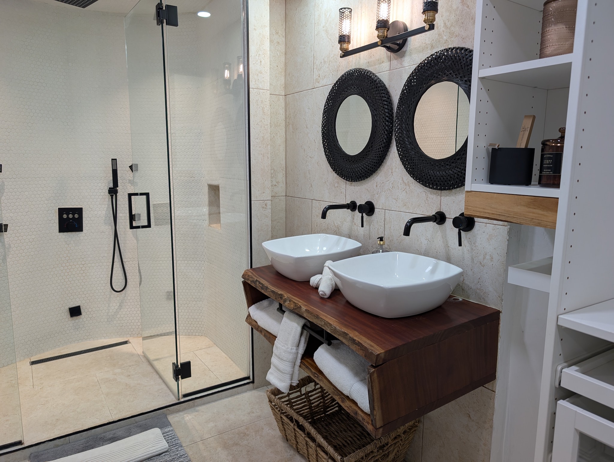 Handmade live-edge mahogany double vanity with white vessel sinks, matte black wall-mounted faucets, industrial lighting, and round black mirrors in the primary bathroom at Villa Coral in Dorado, Puerto Rico
