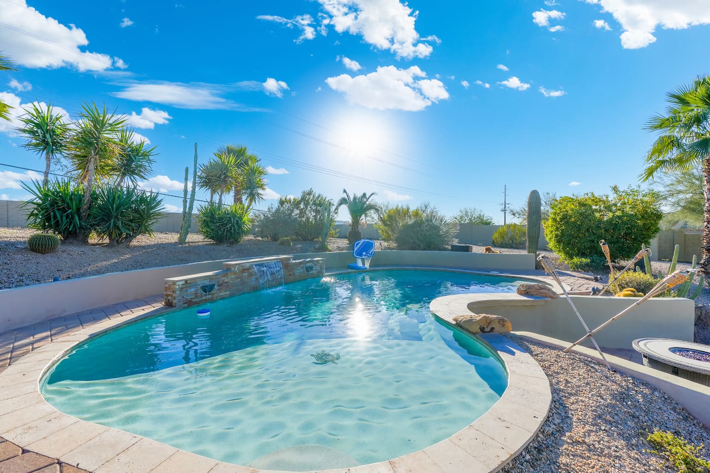 Peaceful poolside scene with clear water, stone accents, and lush desert plants all around.