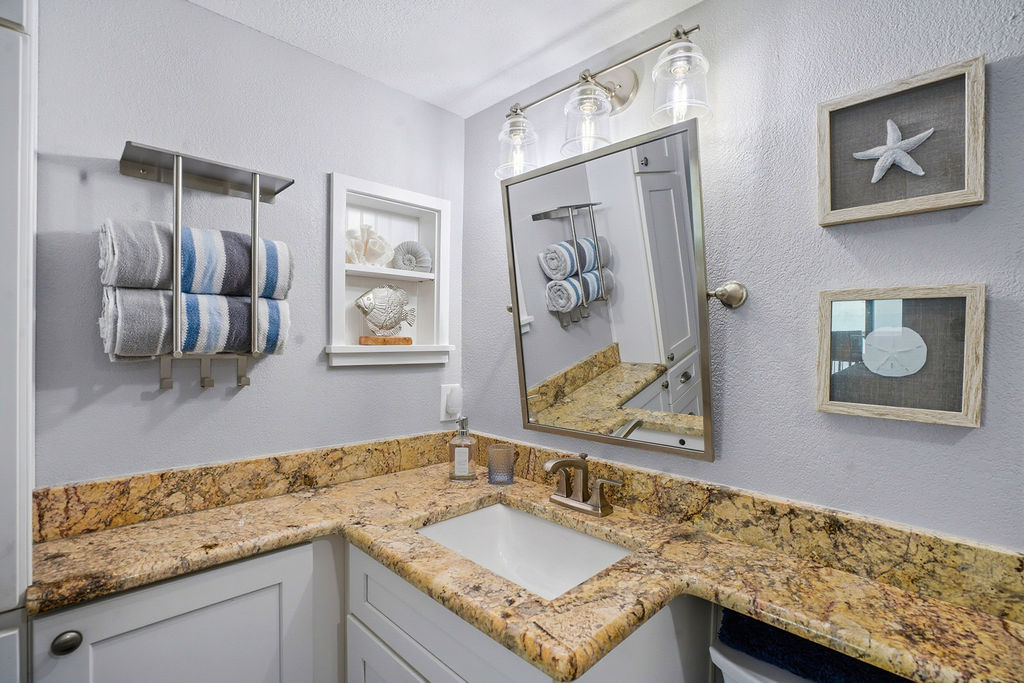 Stylish coastal bathroom vanity featuring granite countertops, modern lighting, towel storage, and beach-inspired décor.