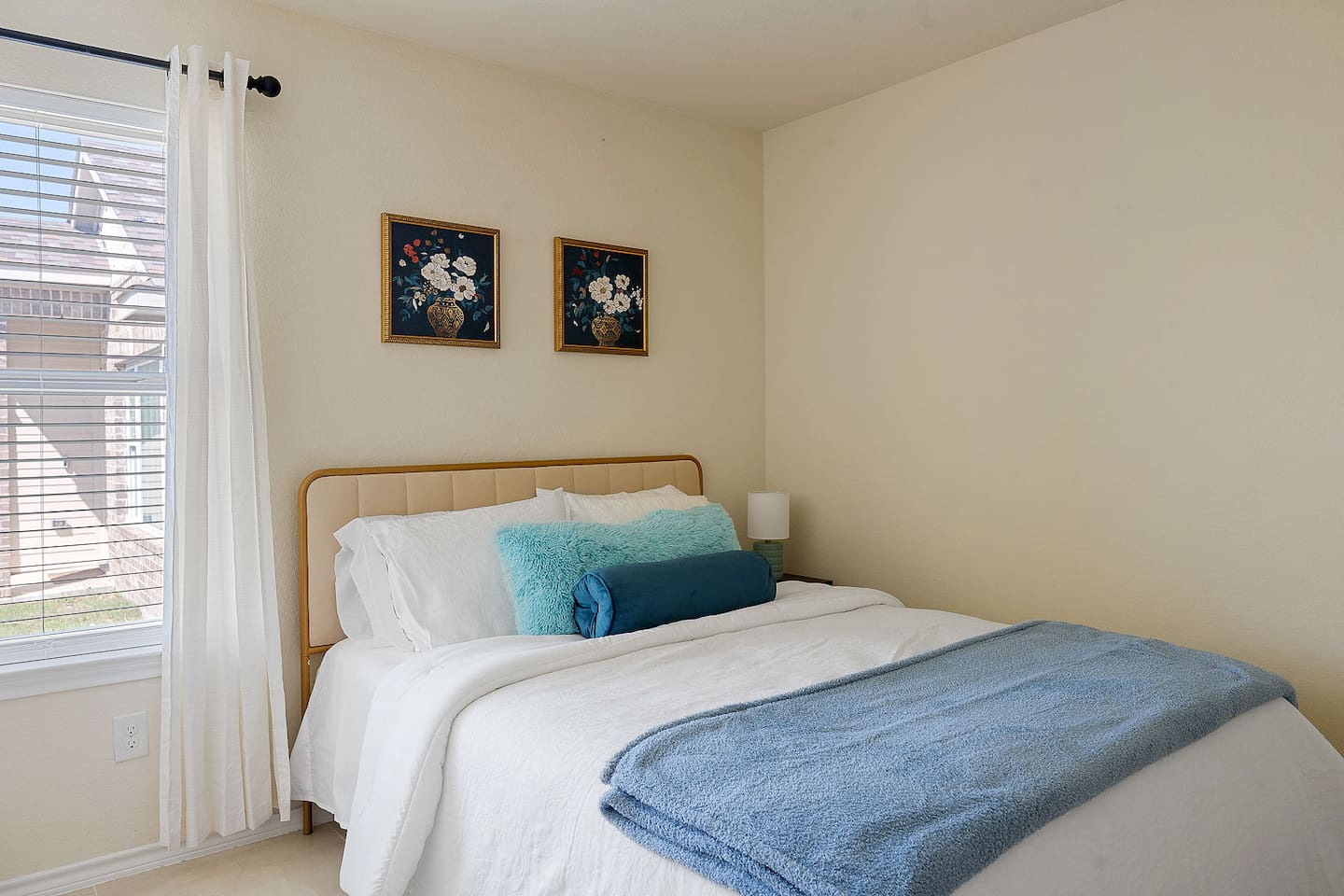 Explore this quaint bedroom including a chic light, a trendy nightstand, and colorful floral artwork.