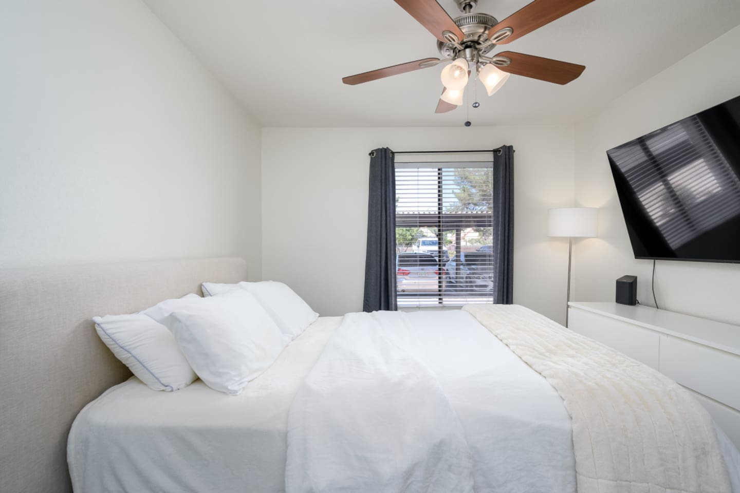 Bedroom with queen bed, wall-mounted TV, ceiling fan, and simple storage for everyday comfort.