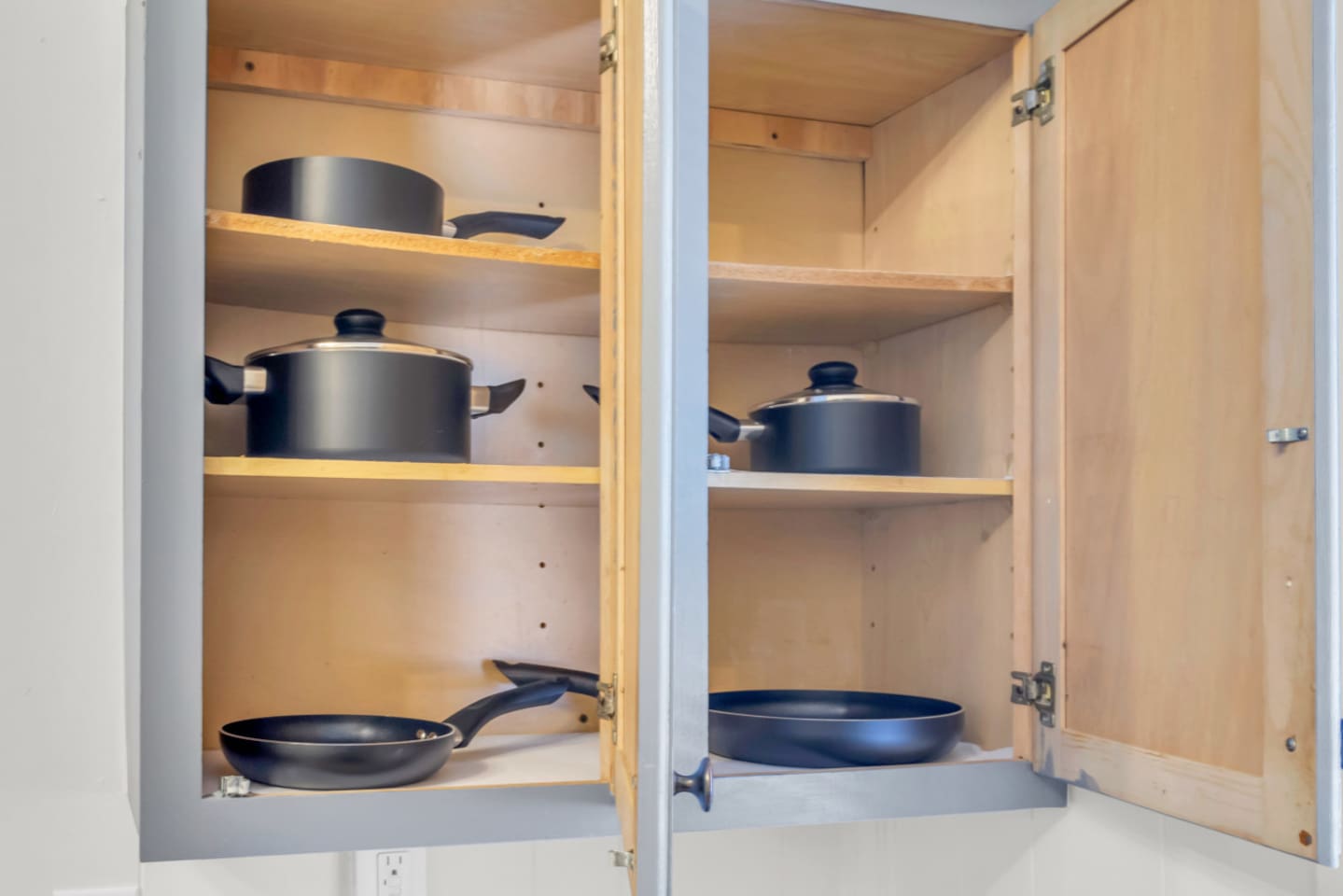 Kitchen cabinet stocked with cookware and essentials.