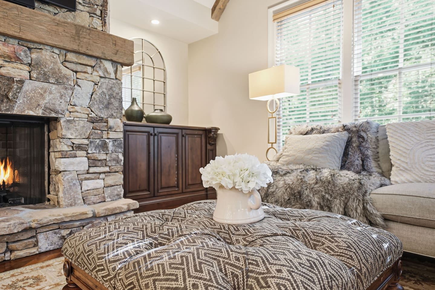 Relax in a warm and welcoming living room featuring high ceilings, a beautiful stone fireplace, and rich wood accents that create a cozy, home-like atmosphere. Enjoy a smart TV with a quality sound system perfect for movie nights and quiet mornings.
