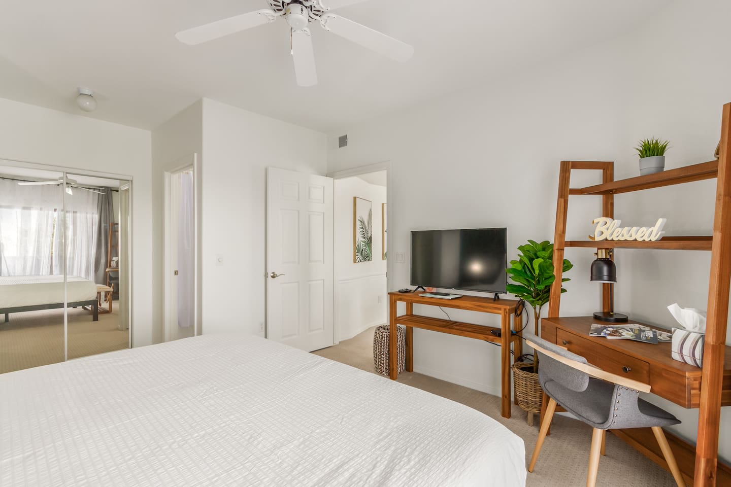 Bedroom with a large bed, dedicated workspace, TV, ceiling fan, and mirrored closet for added storage.
