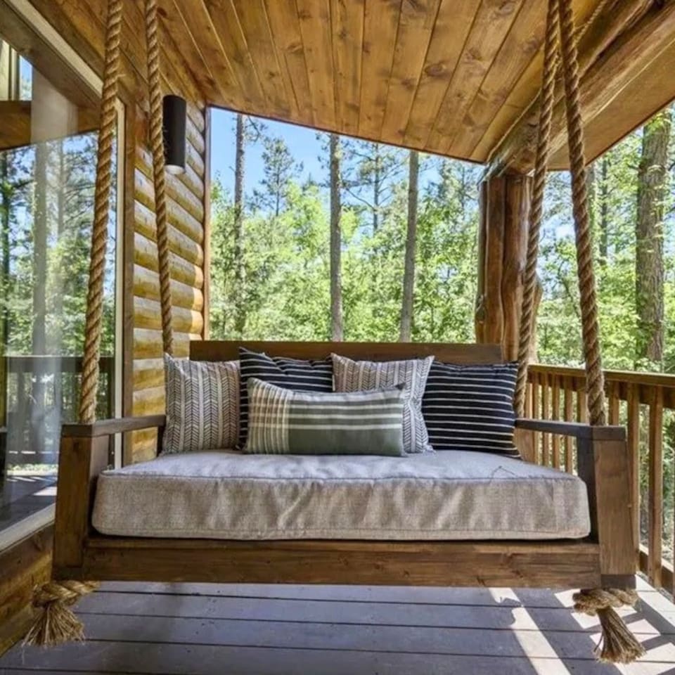 Unwind on the cozy bedded swing under the covered porch, perfect for relaxing afternoons and enjoying peaceful forest views
