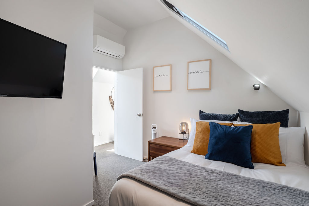 Fernhill Mountain Escape’s upstairs bedroom adds a quiet retreat beneath the skylight, with soft bedding, a reading chair and a small desk nook.