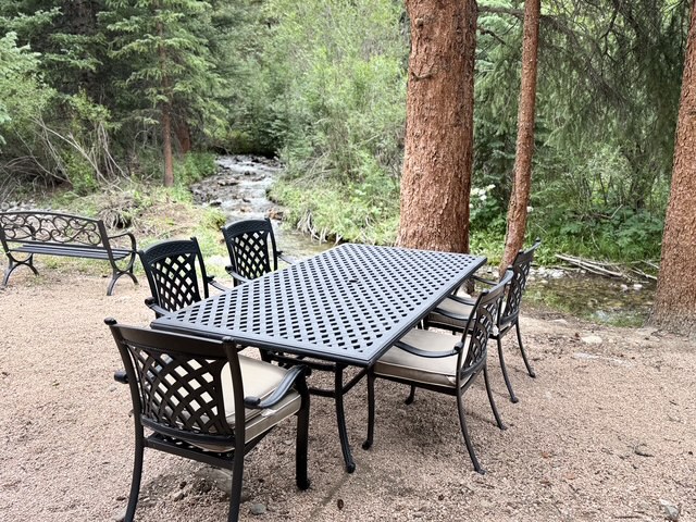 Outdoor dining feels different when the table sits beneath towering trees beside a flowing mountain creek.