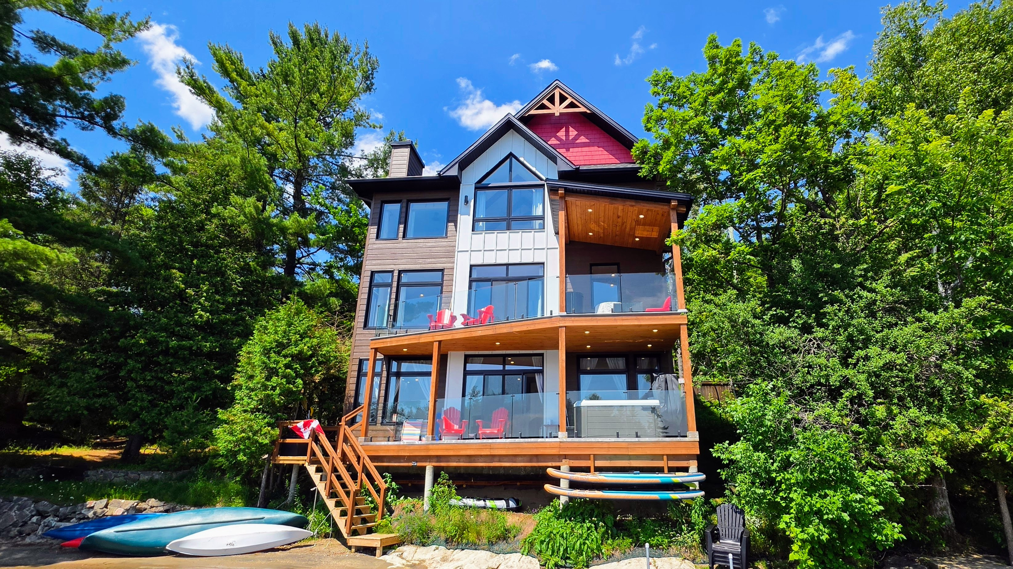 View of cottage from dock showing deck access, hot tub and watercraft stored at front of cottage