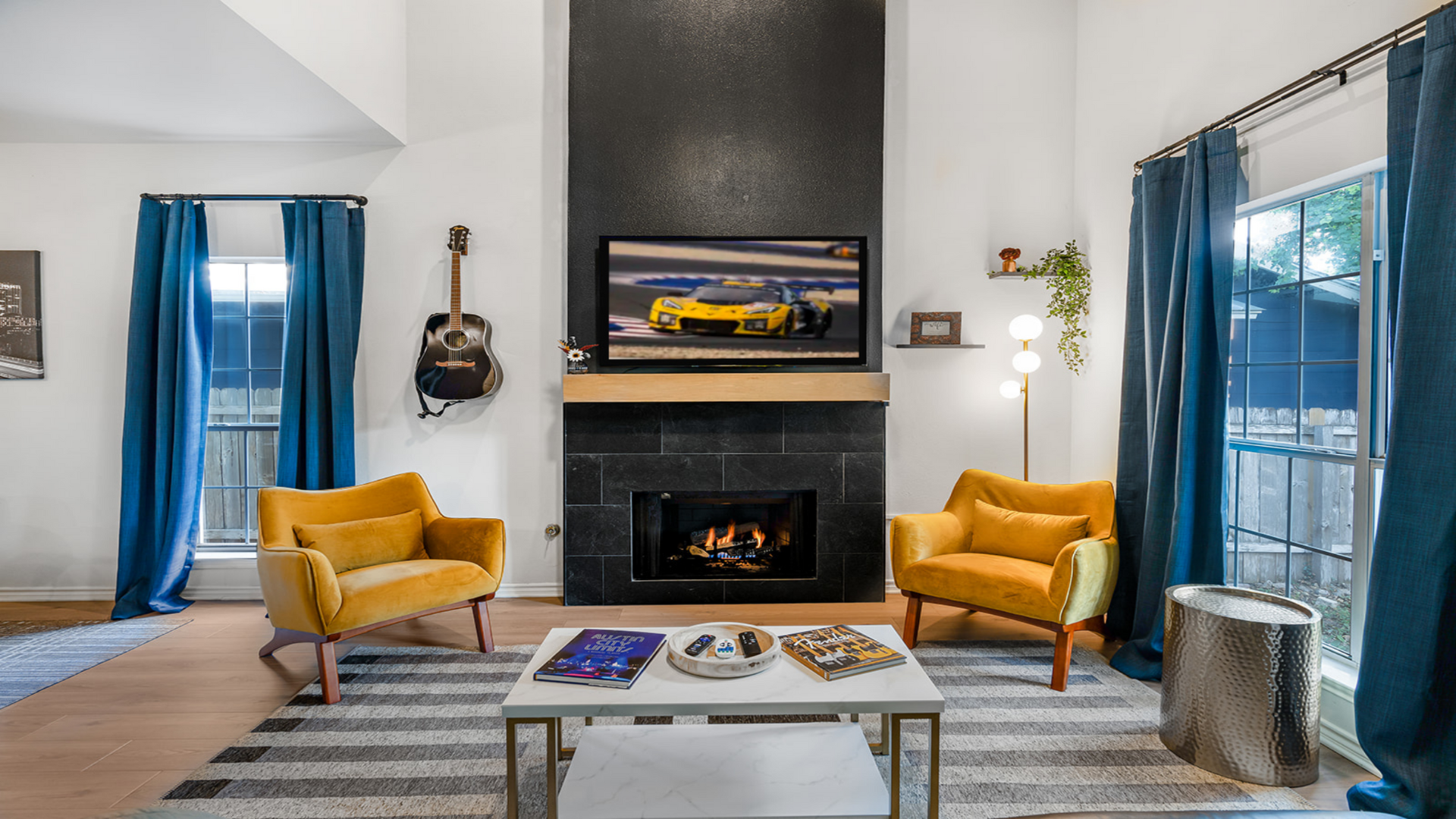 Cozy up by the fireplace in this stylish living room! With bold mustard chairs, a sleek black wall, and COTA on TV, plus a guitar for a jam, it’s the perfect spot to relax and unwind!