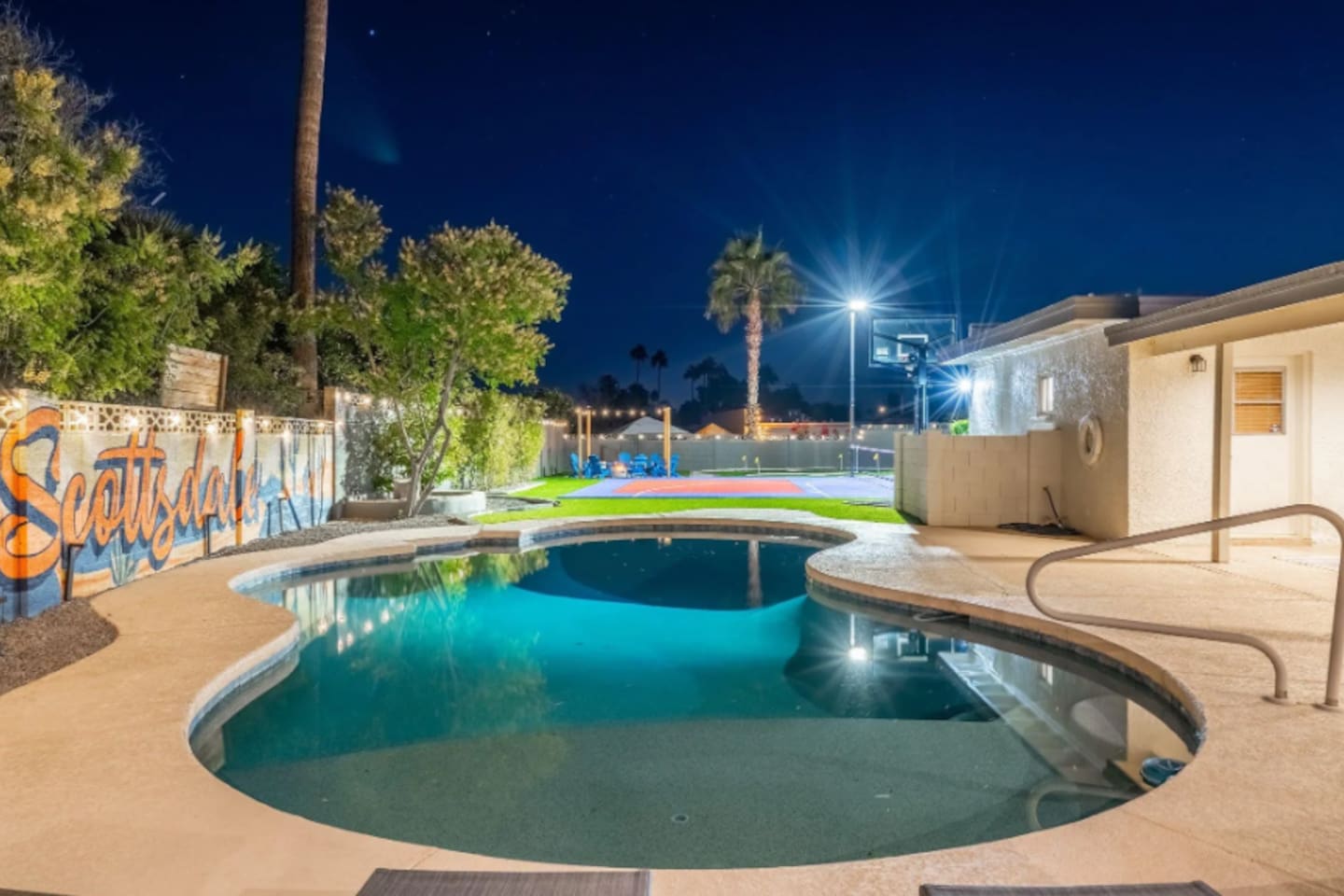 The pool glows at night, with the sport court lit just beyond — pick your pace, the whole backyard is yours.