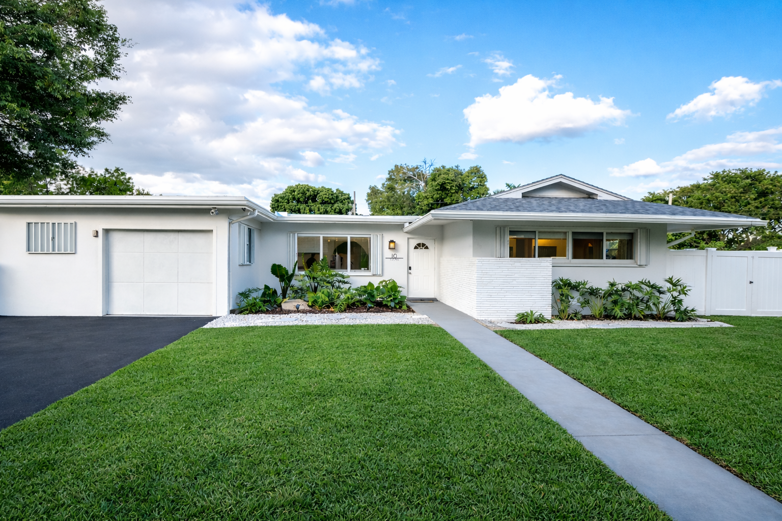 Crisp Palm Beach curb appeal with lush landscaping, private drive, and timeless mid-century charm in a quiet residential neighborhood.