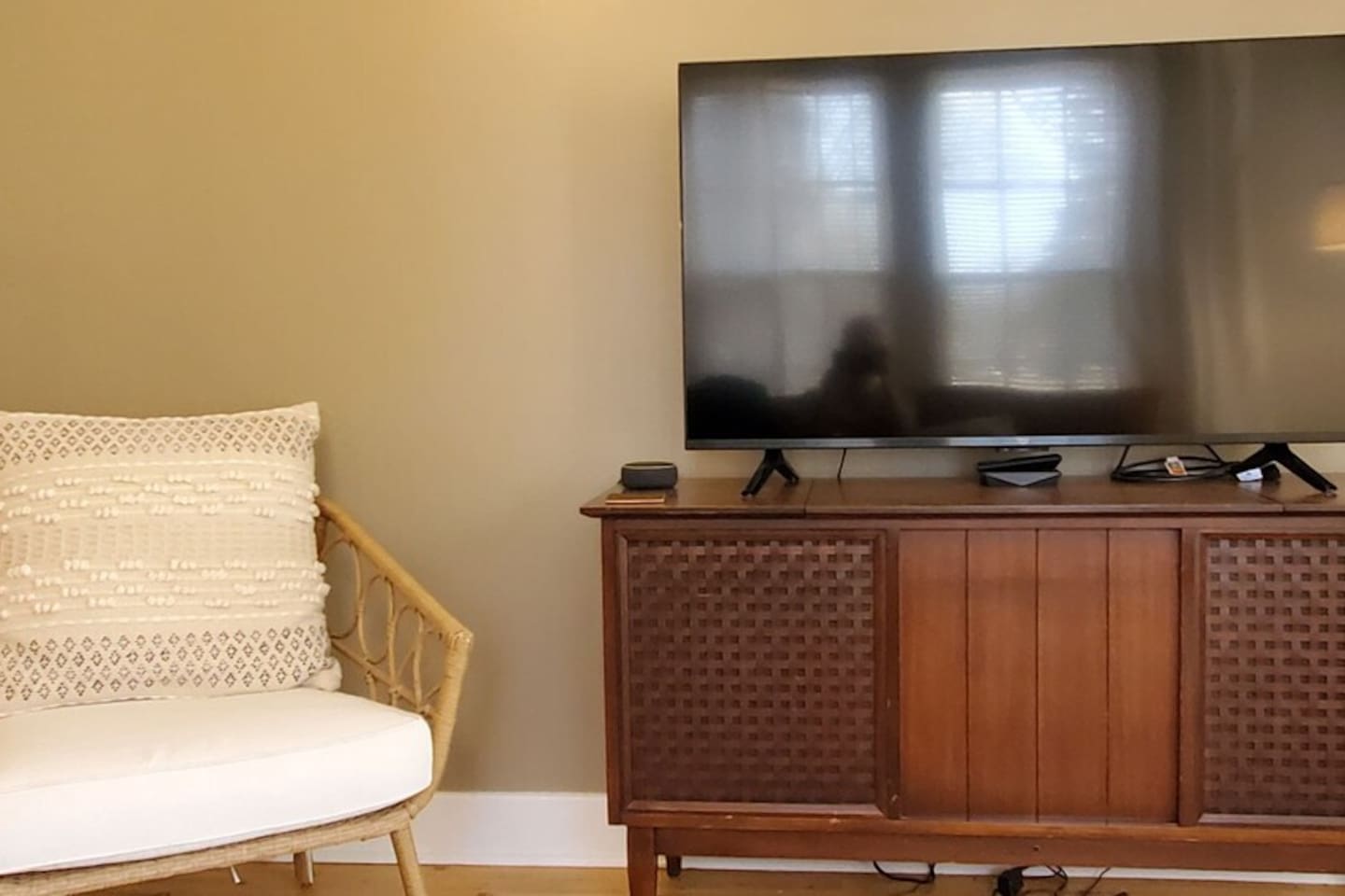 Cozy living area with a flat-screen TV, mid-century console, and a cushioned rattan chair—perfect for relaxing in comfort and style.