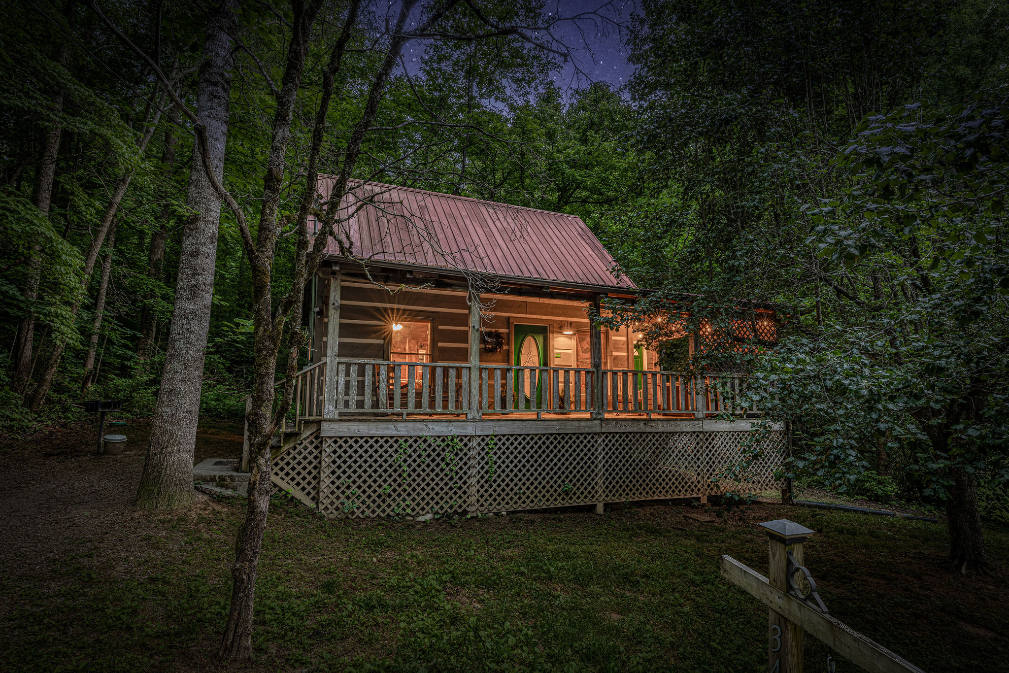 Porch lit up, trees all around, evening starting right.