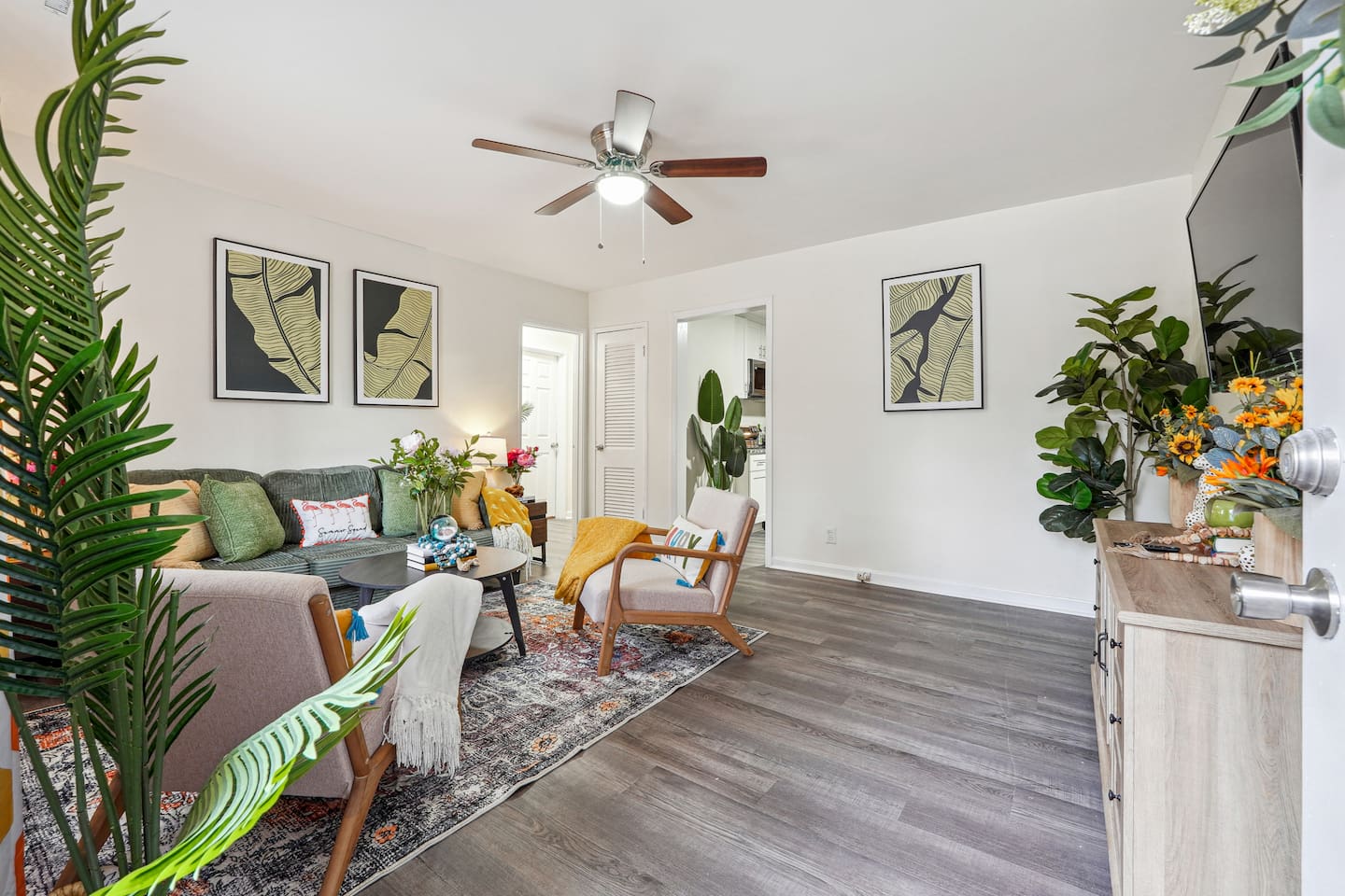 Enjoy a cozy living room featuring a long comfortable sofa, a TV for your entertainment, a ceiling fan, two chair, and a window with a lovely view outside — perfect for relaxing and unwinding.
