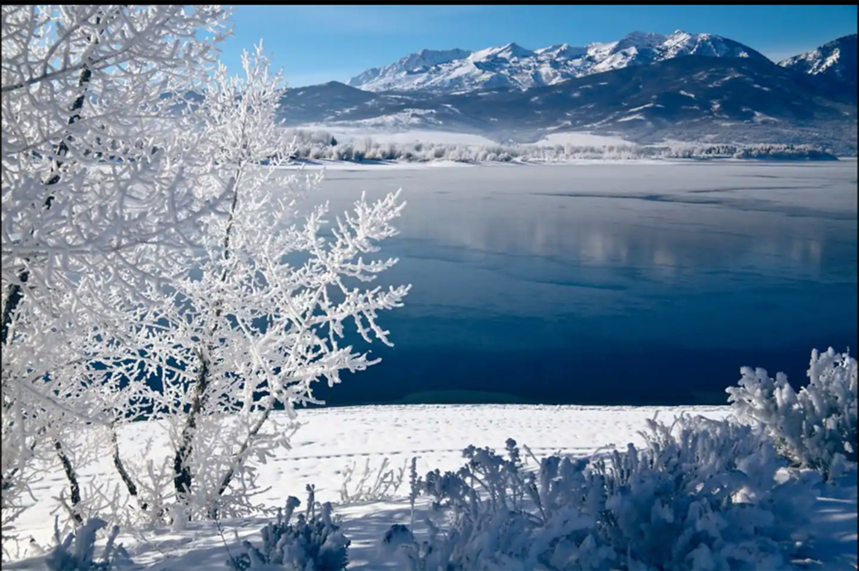 Experience peaceful winter mornings by the frozen lake, surrounded by snow-covered trees and mountain peaks.