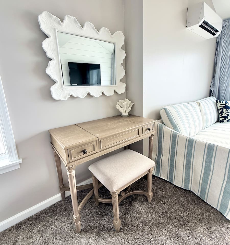 Get ready at this charming, light-toned wooden vanity paired with a matching upholstered stool, providing a stylish and functional spot for your daily routine or workstation in this cozy space.