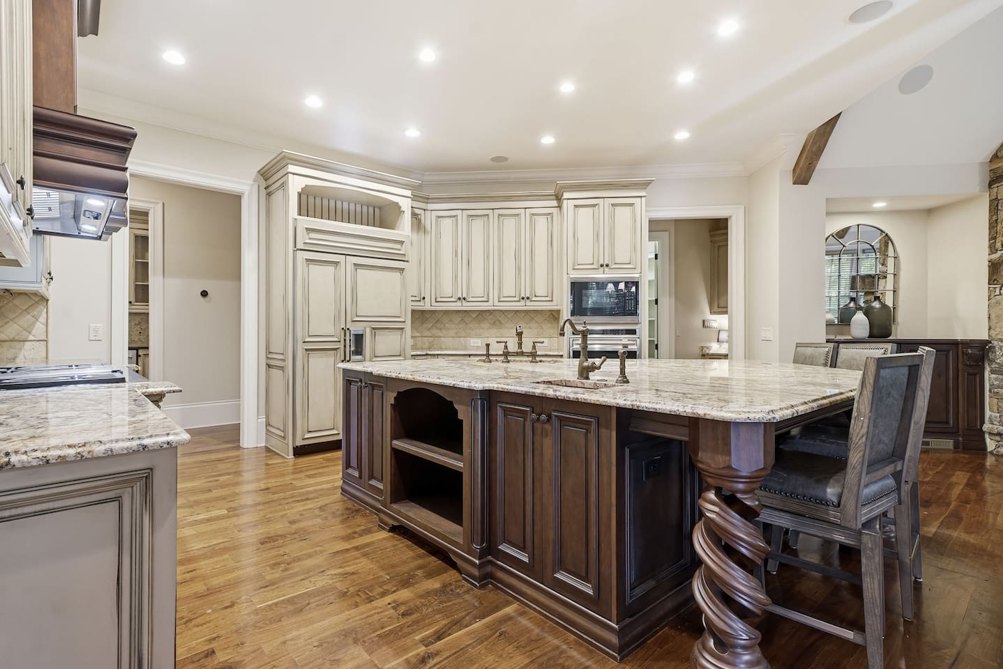 This open kitchen features beautiful cream wood cabinetry, sleek granite countertops, and an island that comfortably seats four. The bright, airy design makes it the perfect place to cook, gather, and share meals together.