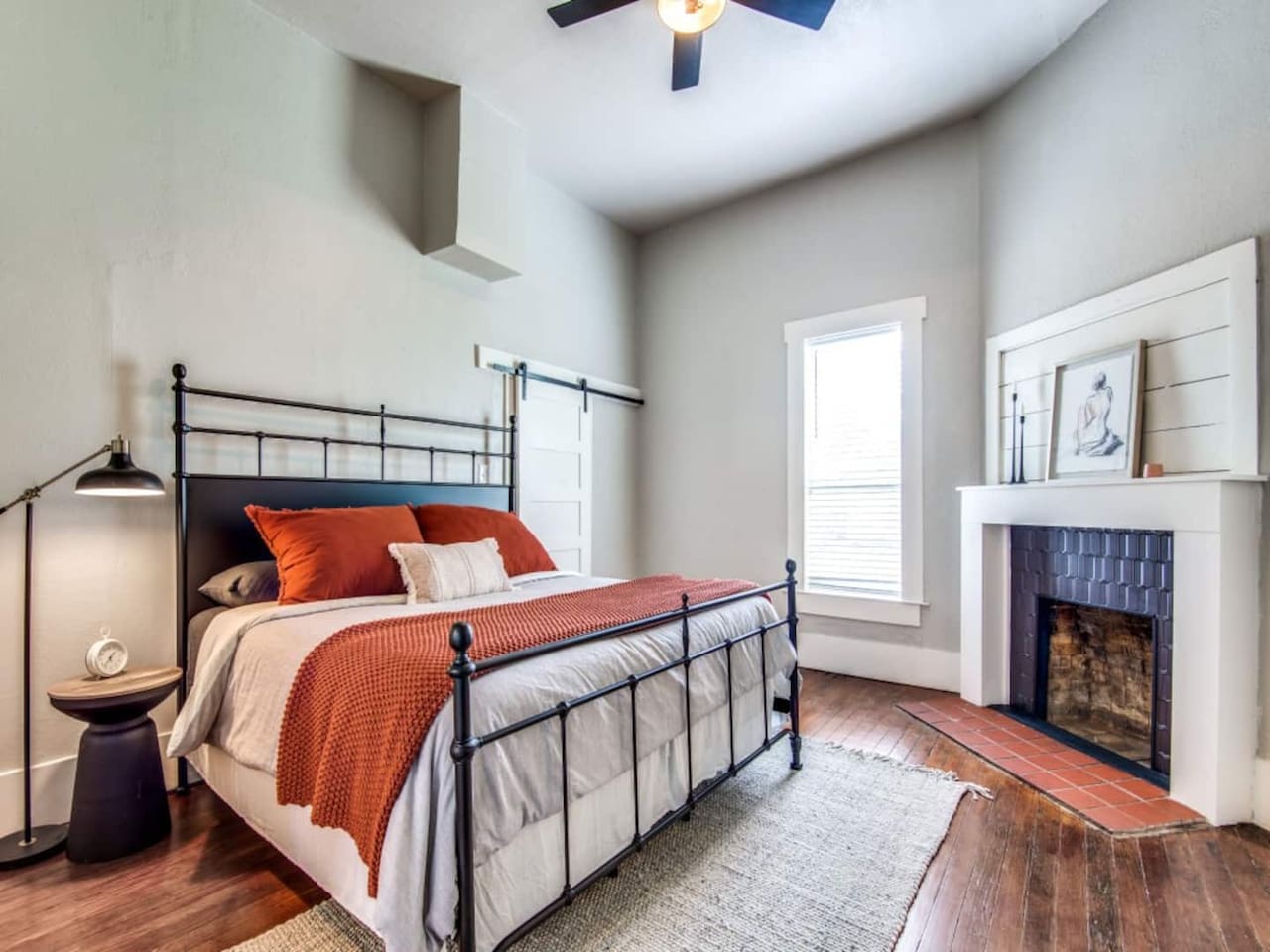 King primary suite with iron-frame bed, terracotta bedding, hardwood floors, ceiling fan, and decorative fireplace. Private ensuite bathroom included. Modern farmhouse Airbnb steps from downtown Aubrey TX near Denton County wedding venues.