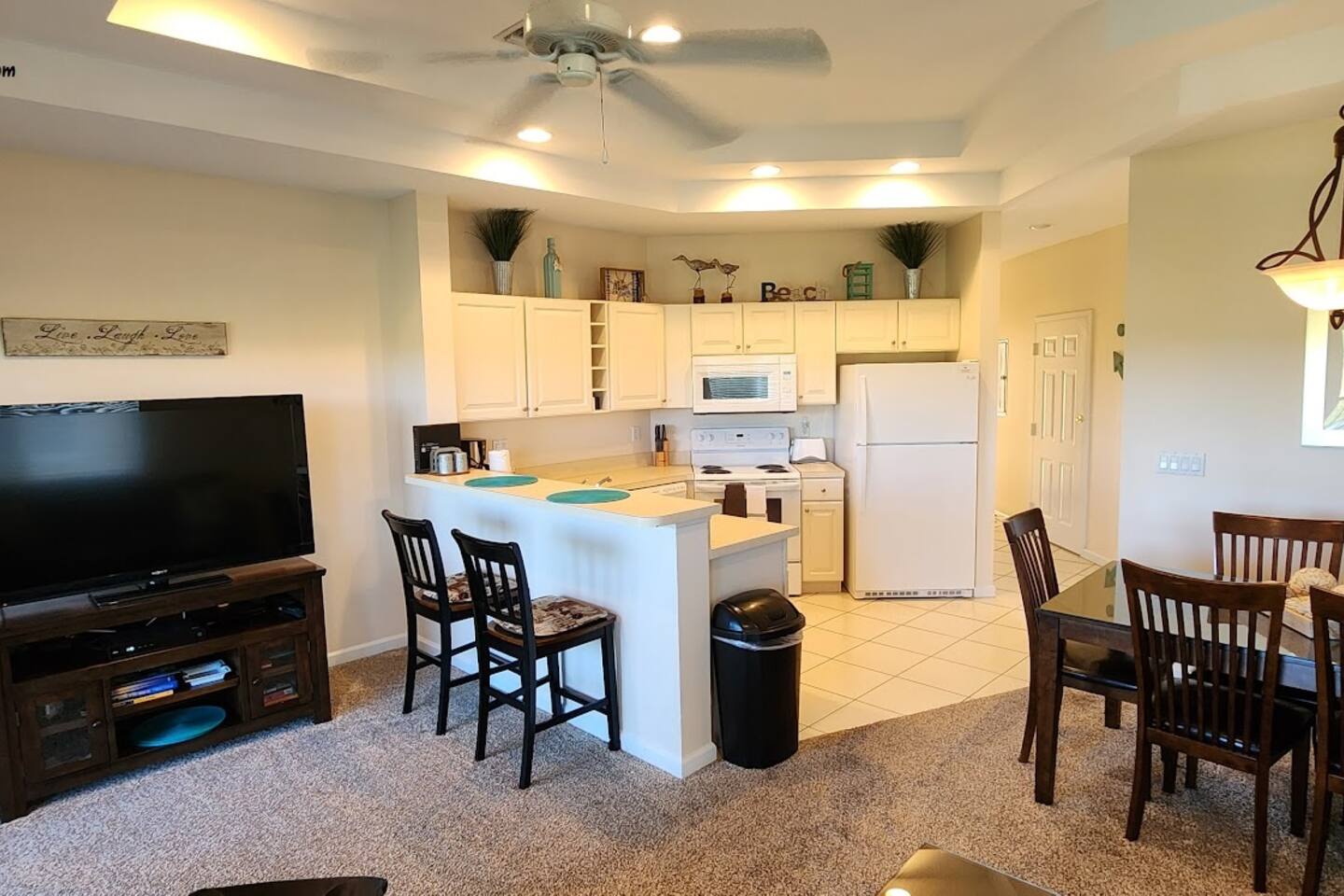 Bright kitchen and living space with breakfast bar seating, dining area, large TV, and an open layout perfect for relaxing.