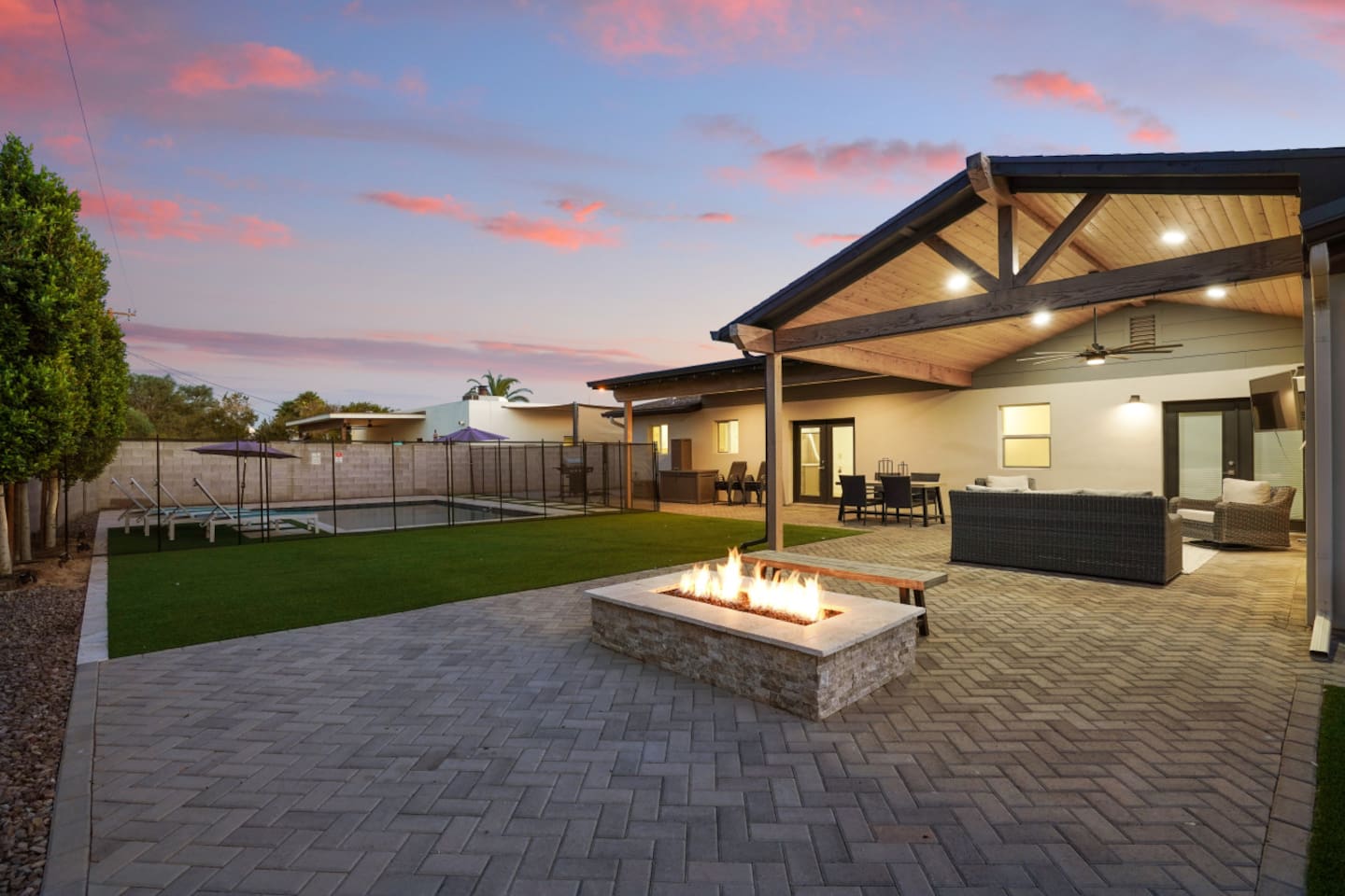 Backyard with fire pit, covered lounge seating, pool, outdoor dining, and TV for easy indoor-outdoor relaxation.