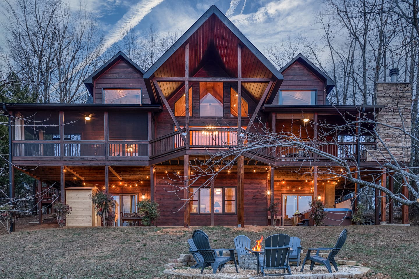 The back of the beautiful "Blessed Sunset" mountain retreat home overlooking the back yard! Stunning A-frame, wrap-around porch, screened-in patio, outdoor fireplace, outdoor dining table, sauna, hot tub, outdoor couch, and more!