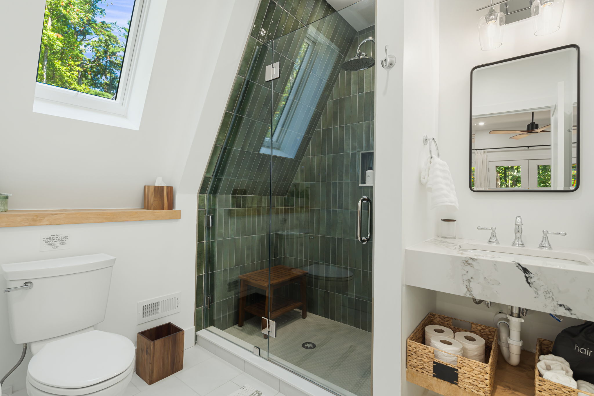 The 2nd floor ensuite bath features a skylight, flooding the space with natural light. It includes a walk-in, contemporary, tile-surround shower with a rain showerhead and practical shower wand. A medicine cabinet and floating vanity completes the space.