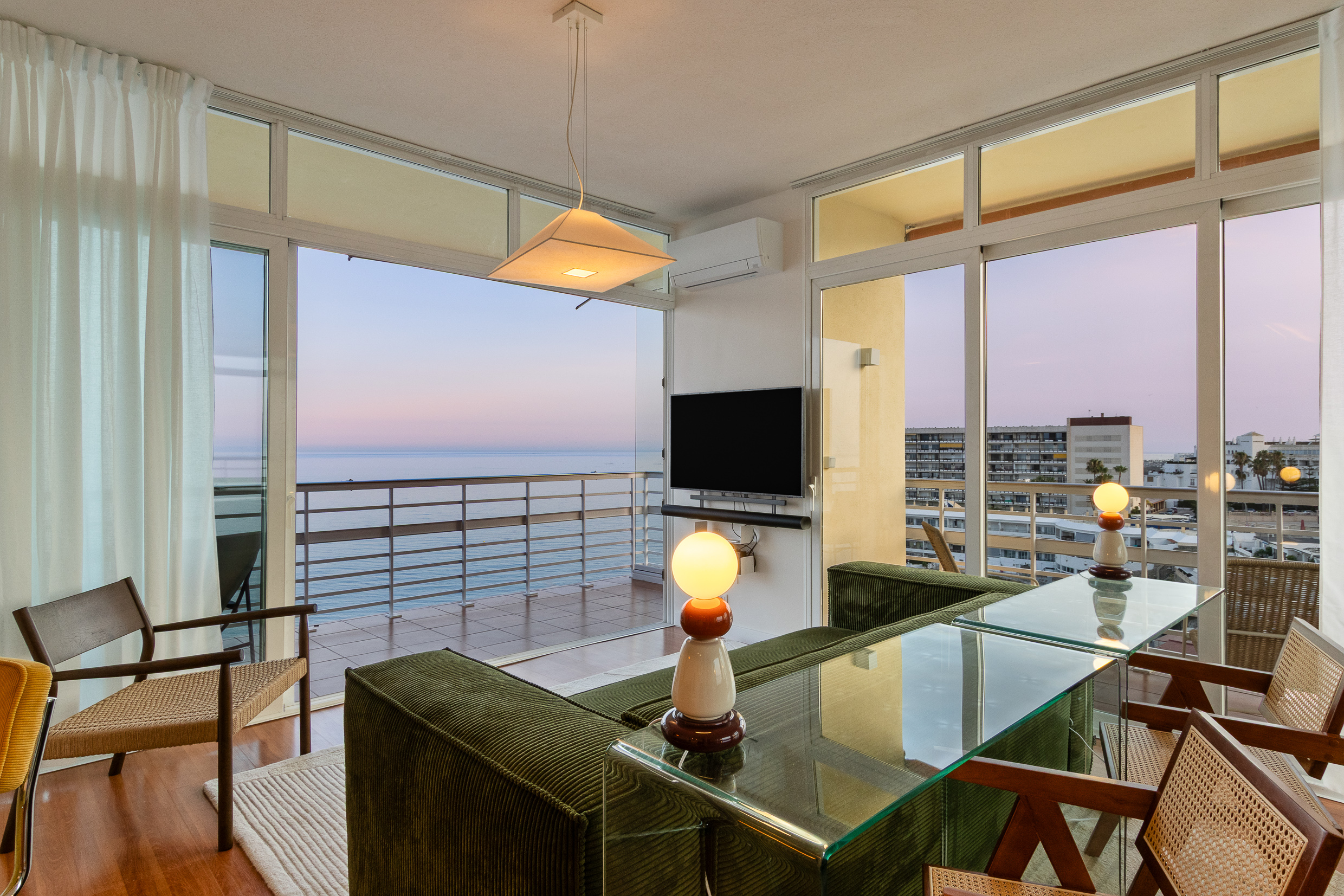 Indoor-outdoor living with an open balcony, sea views and warm evening light.